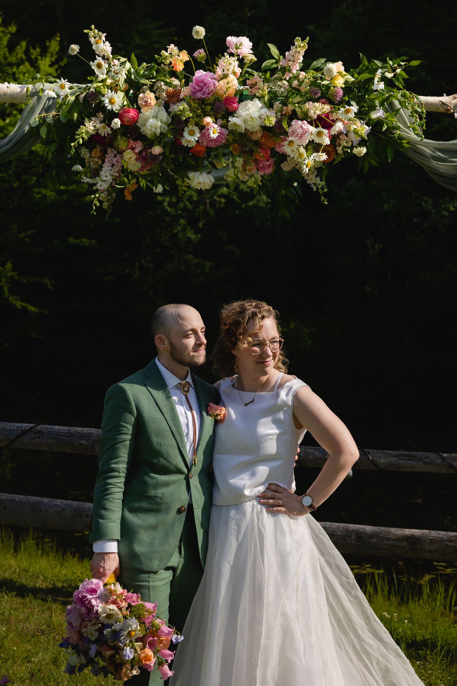 A wedding ceremony arch decorated with lush pink and white floral arrangements in an outdoor garden setting.