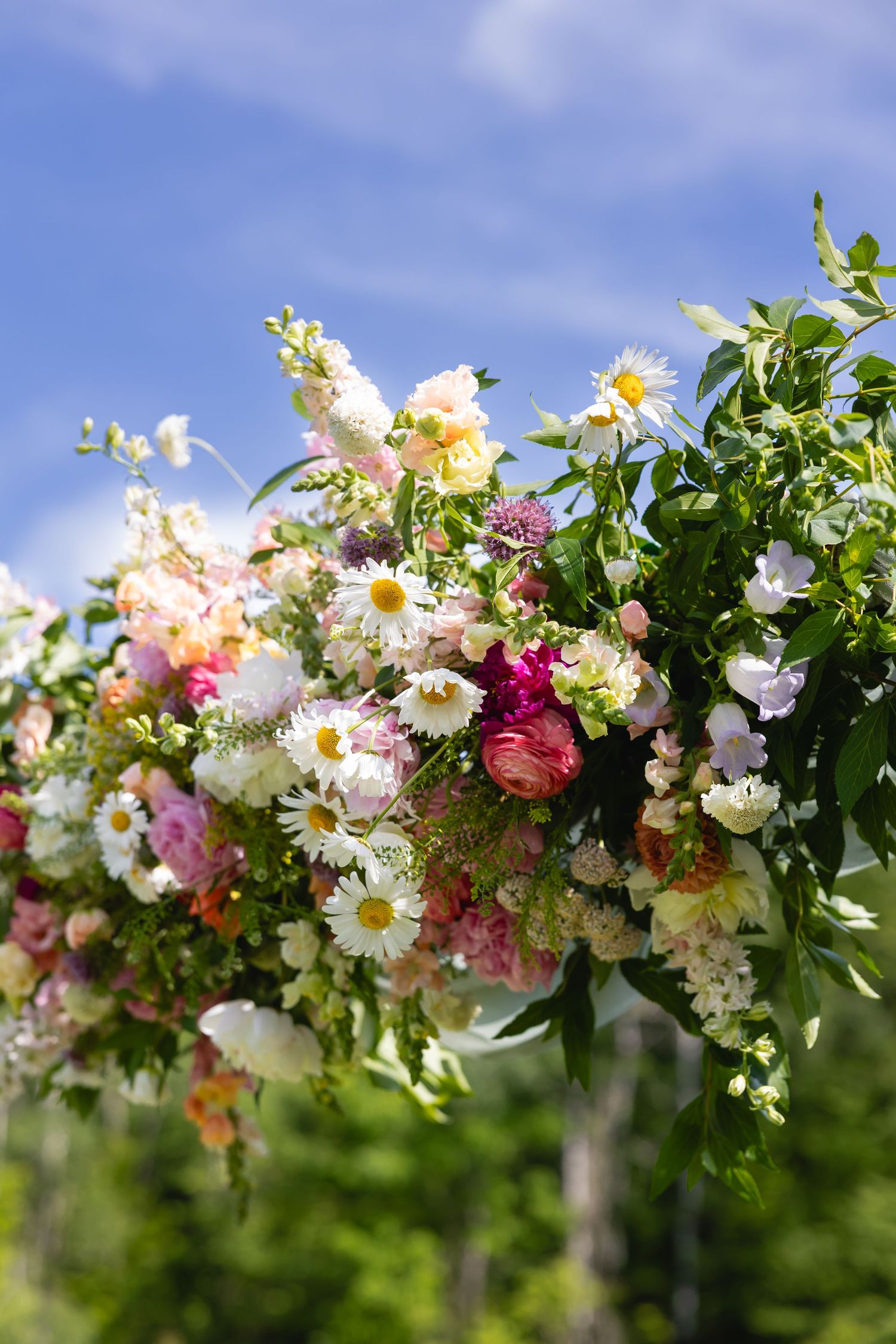 A romantic floral arch arrangement with pink, white, and green blooms against a bright blue summer sky.