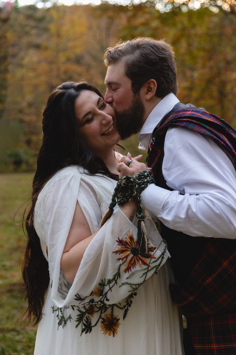 A couple shares a romantic moment in Celtic wedding attire among autumn trees.