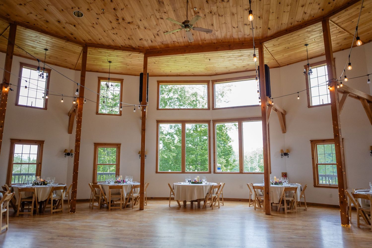 A bright rustic wedding venue interior with high windows, wooden floors and string lights.