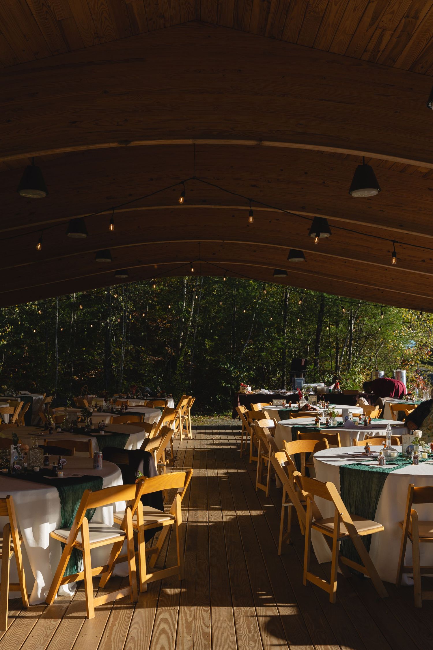 Rustic wooden tables and chairs set up in an elegant covered outdoor dining area with warm ambient lighting.