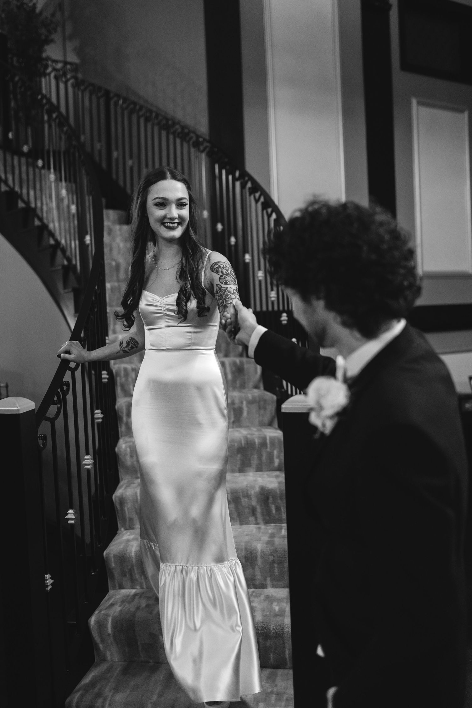 A joyful first look moment captured in black and white as a bride descends an elegant staircase.