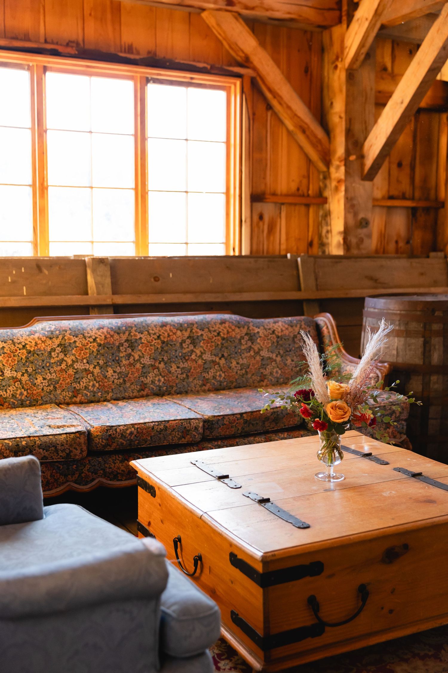 Rustic wooden interior with floral patterned bench seating, trunk coffee table and window in warm sunlight.