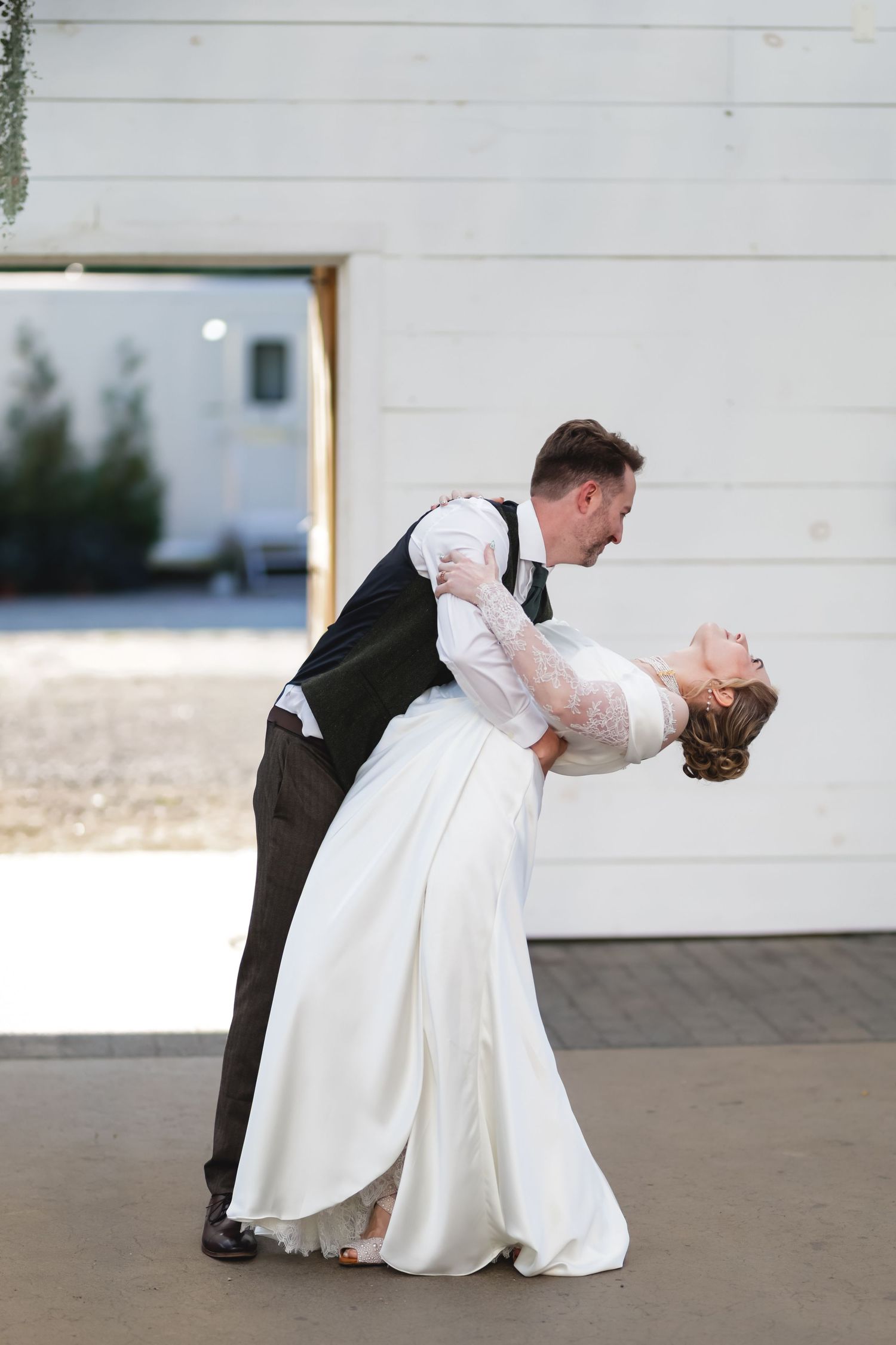 A romantic wedding couple performs a traditional dip pose during their dance on an outdoor patio.