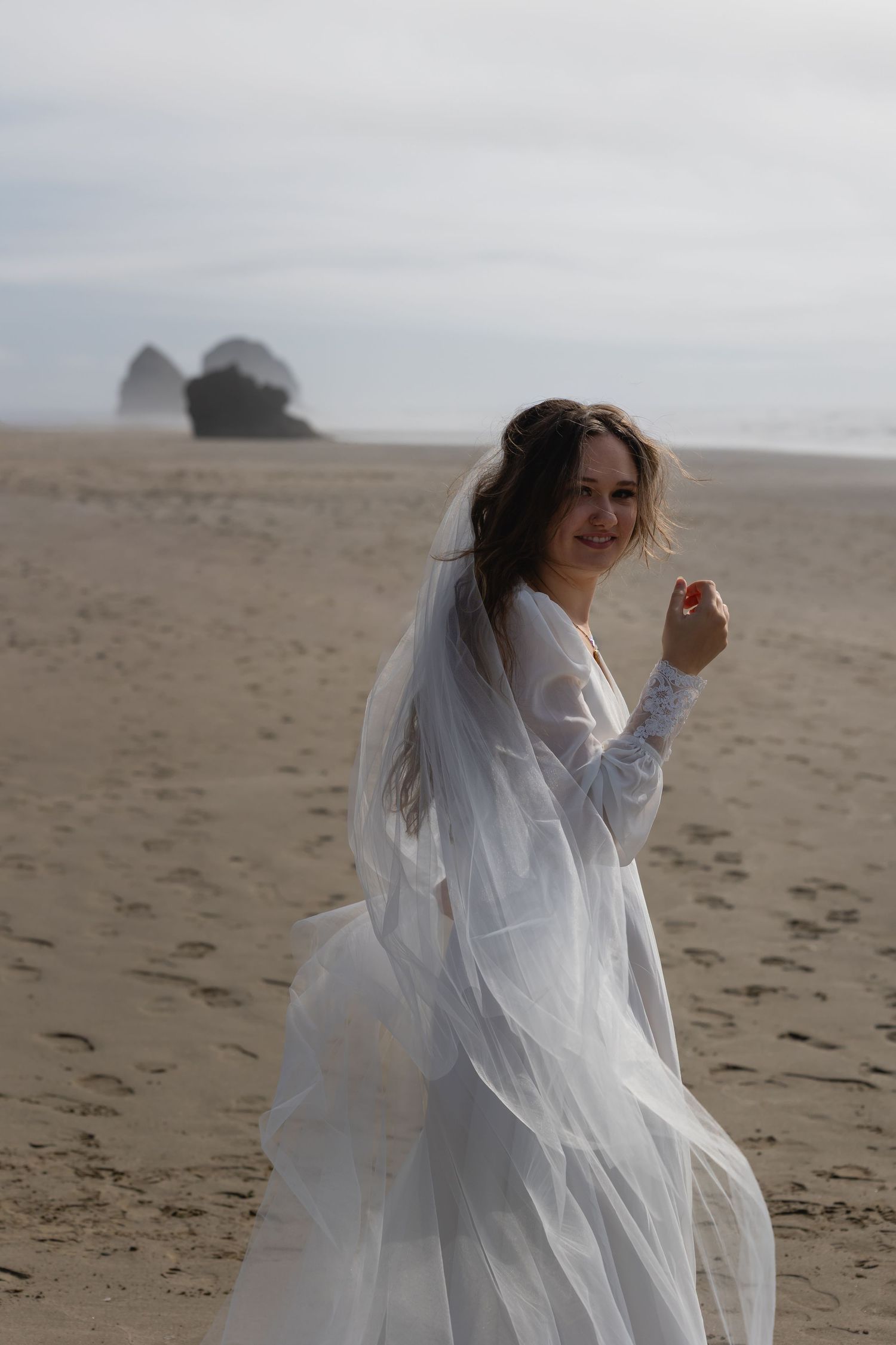 A person in a flowing white dress twirls joyfully on a misty beach with dramatic coastal rock formations in the background.
