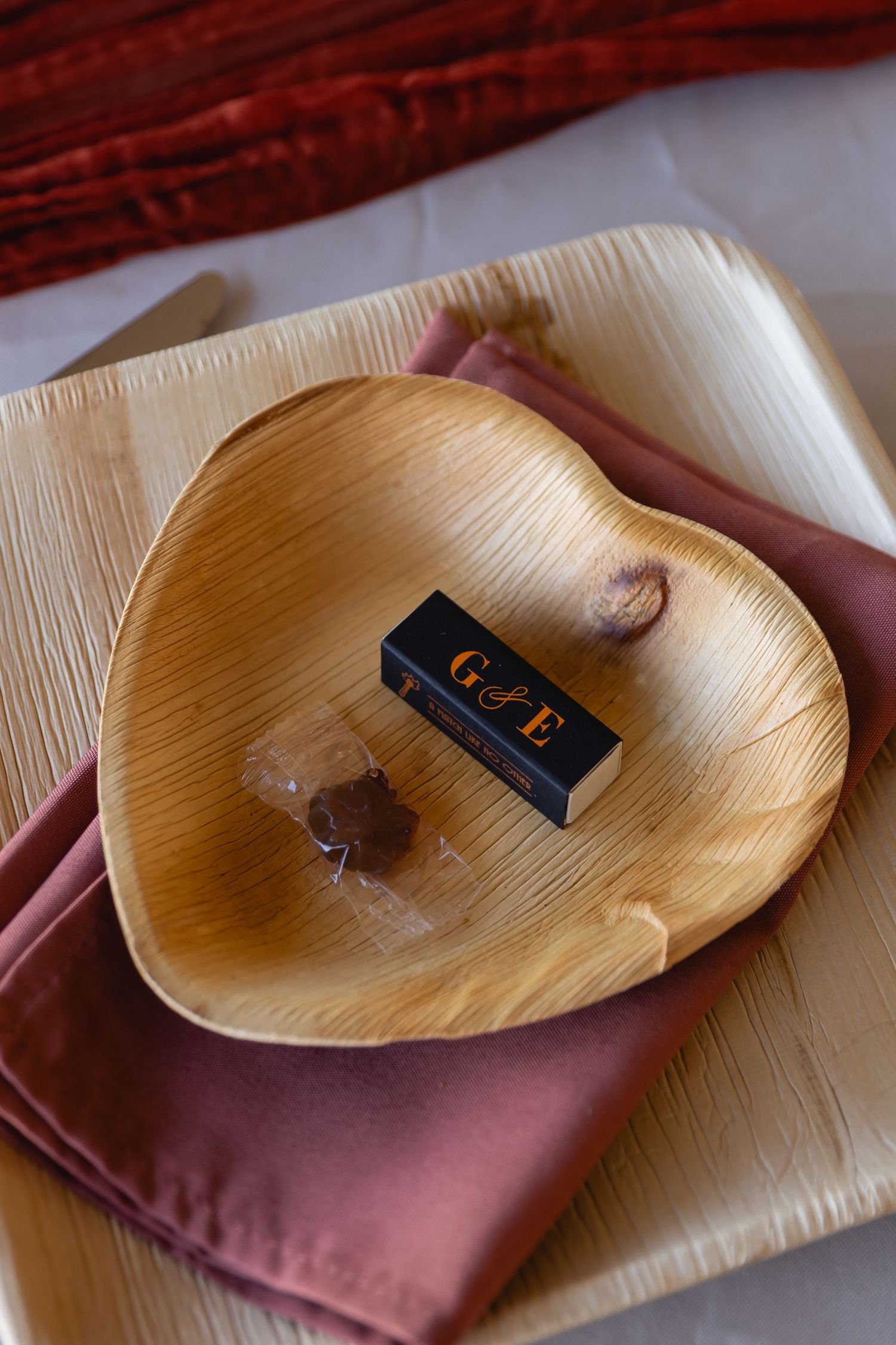 A sequence showing a small black matchbox being placed on a palm-shaped wooden leaf plate with burgundy napkin underneath.