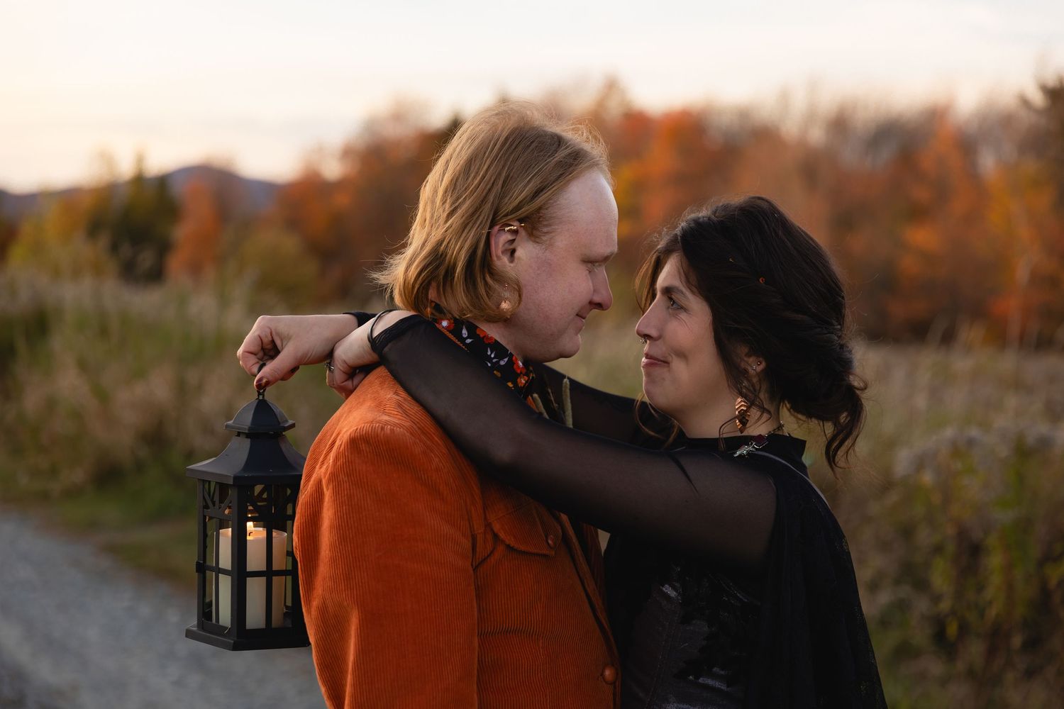 A romantic couple in autumn attire embraces in a golden-lit outdoor setting at sunset.