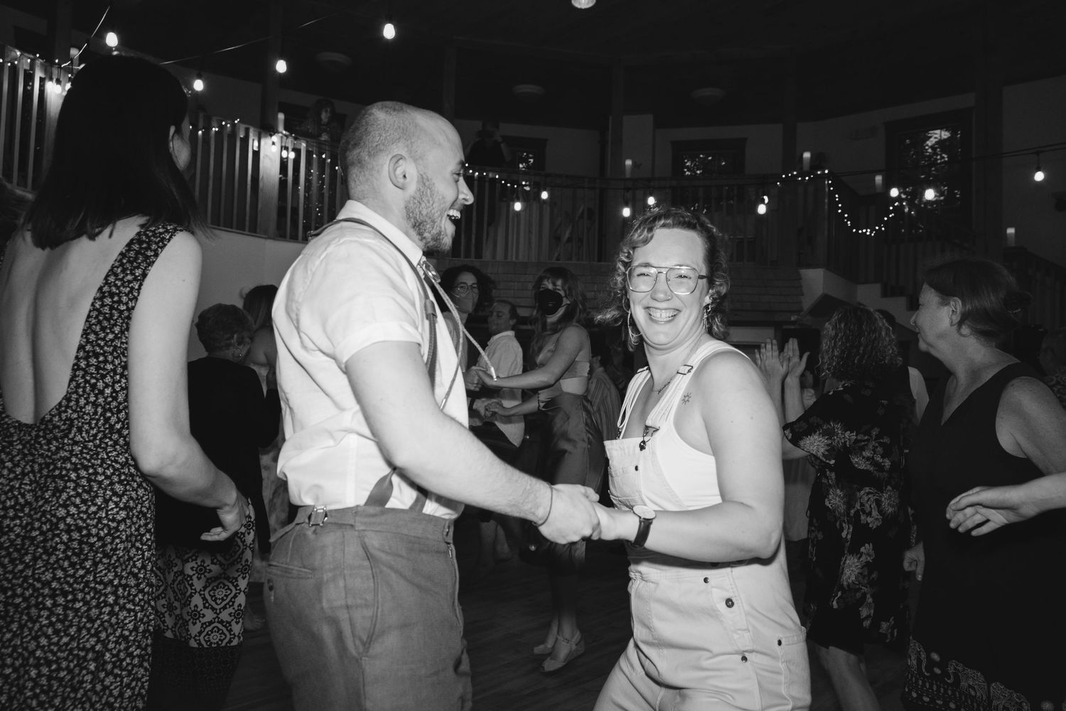 Dancers enjoy themselves on a dimly lit dance floor with string lights overhead at a celebration event.