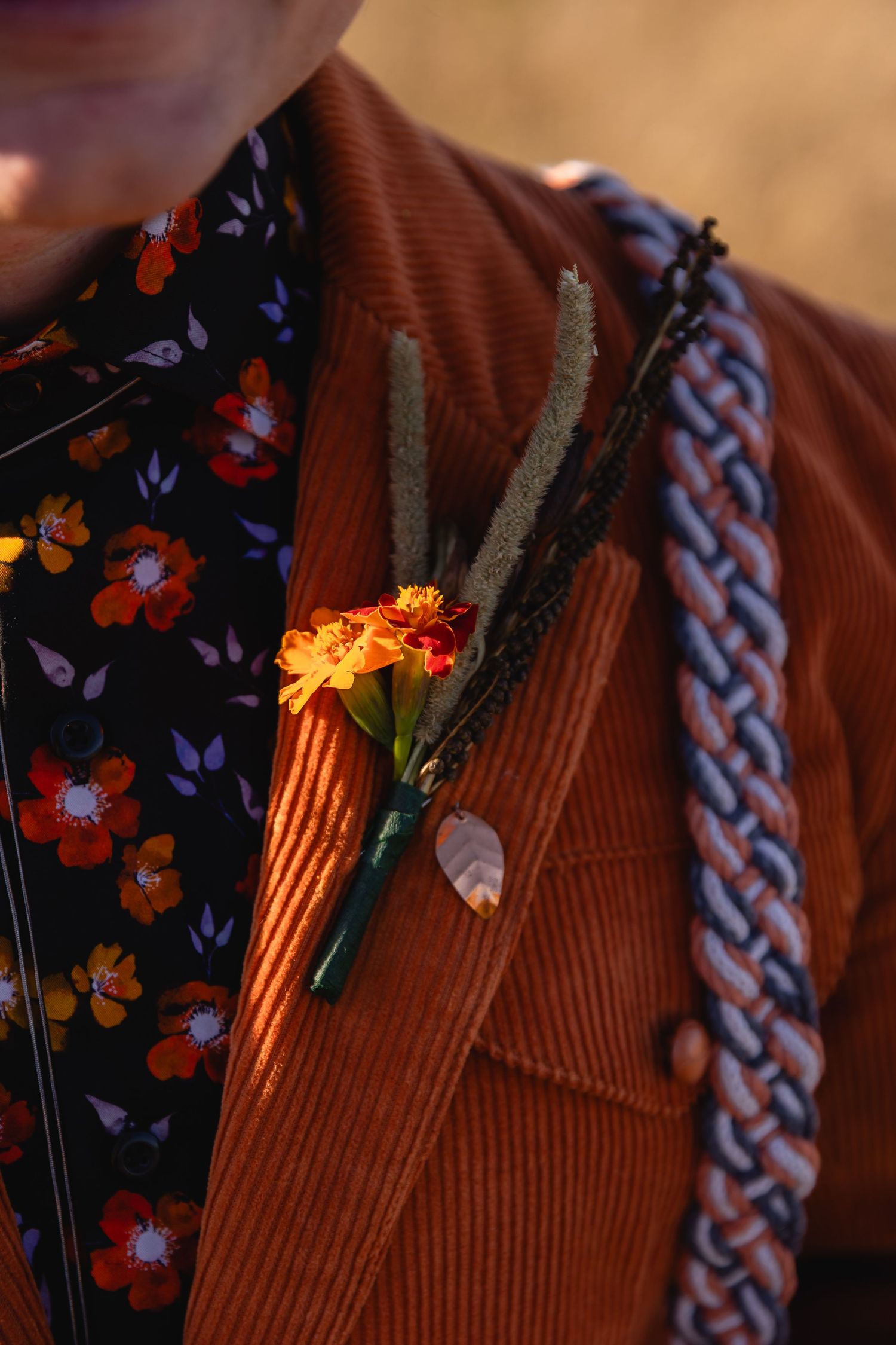Close-up details of a brown corduroy jacket with floral fabric and braided trim in warm lighting.