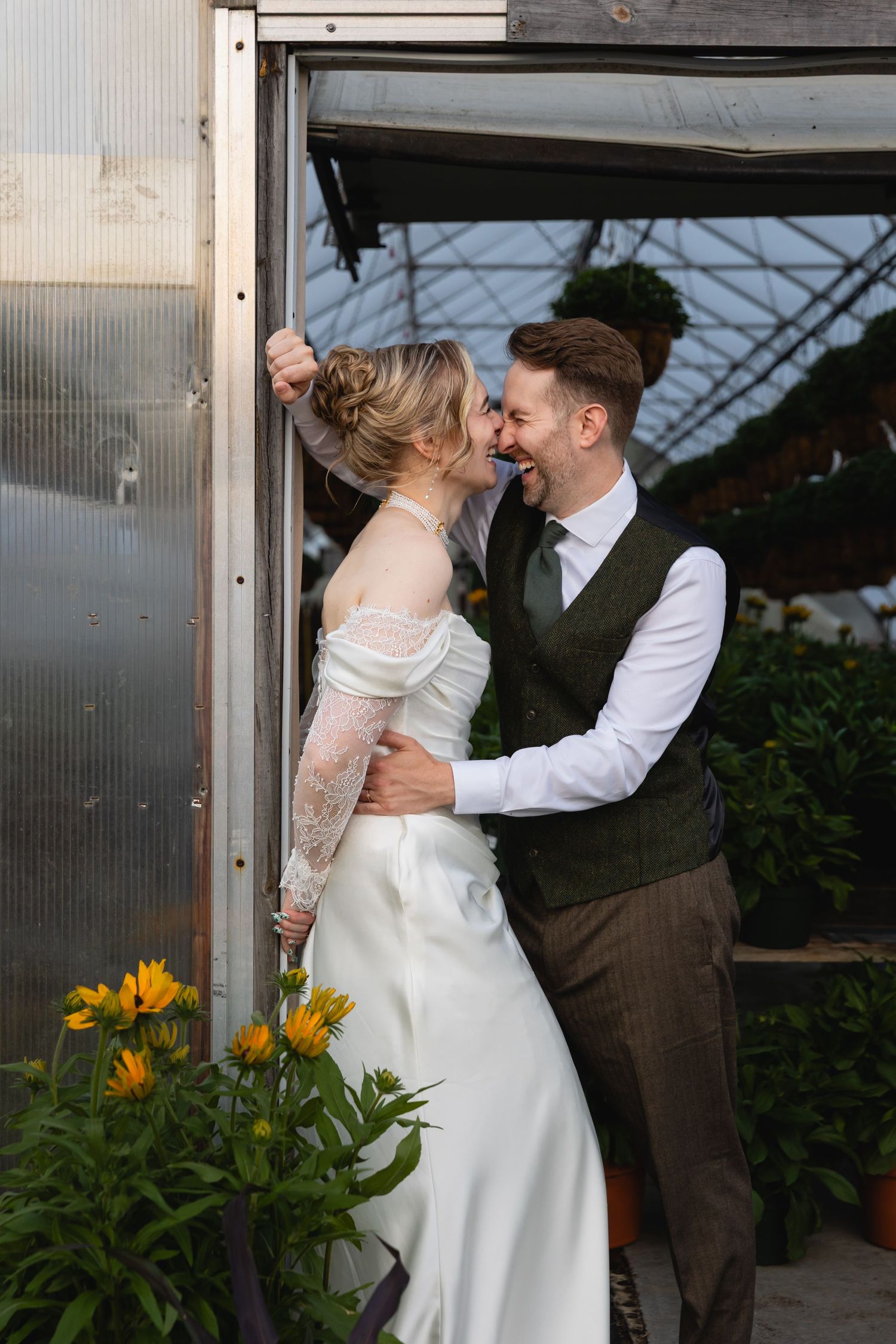 Romantic wedding couple embraces in a greenhouse setting with sunflowers and natural light.