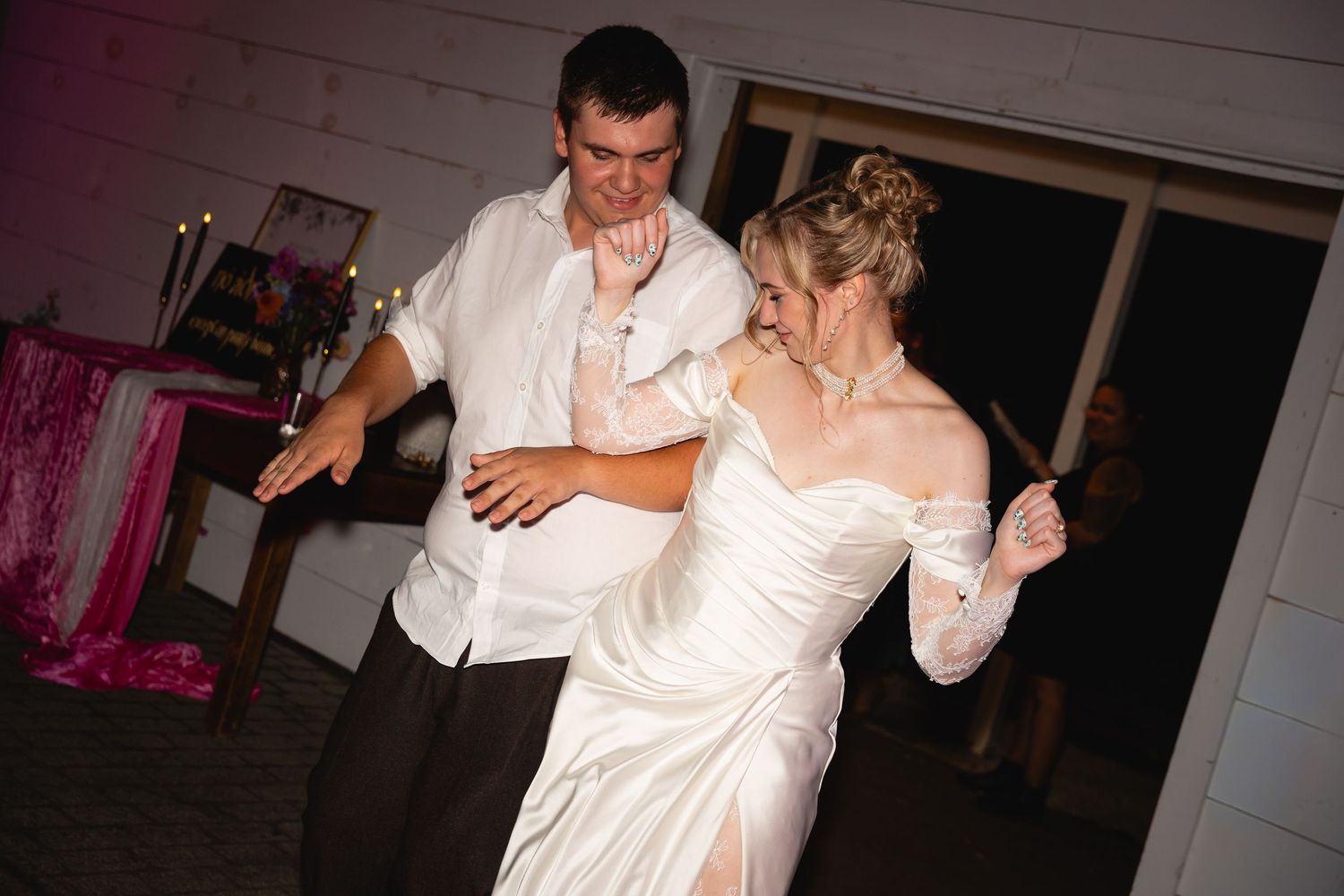Couple dancing together in formal white attire at a wedding reception.