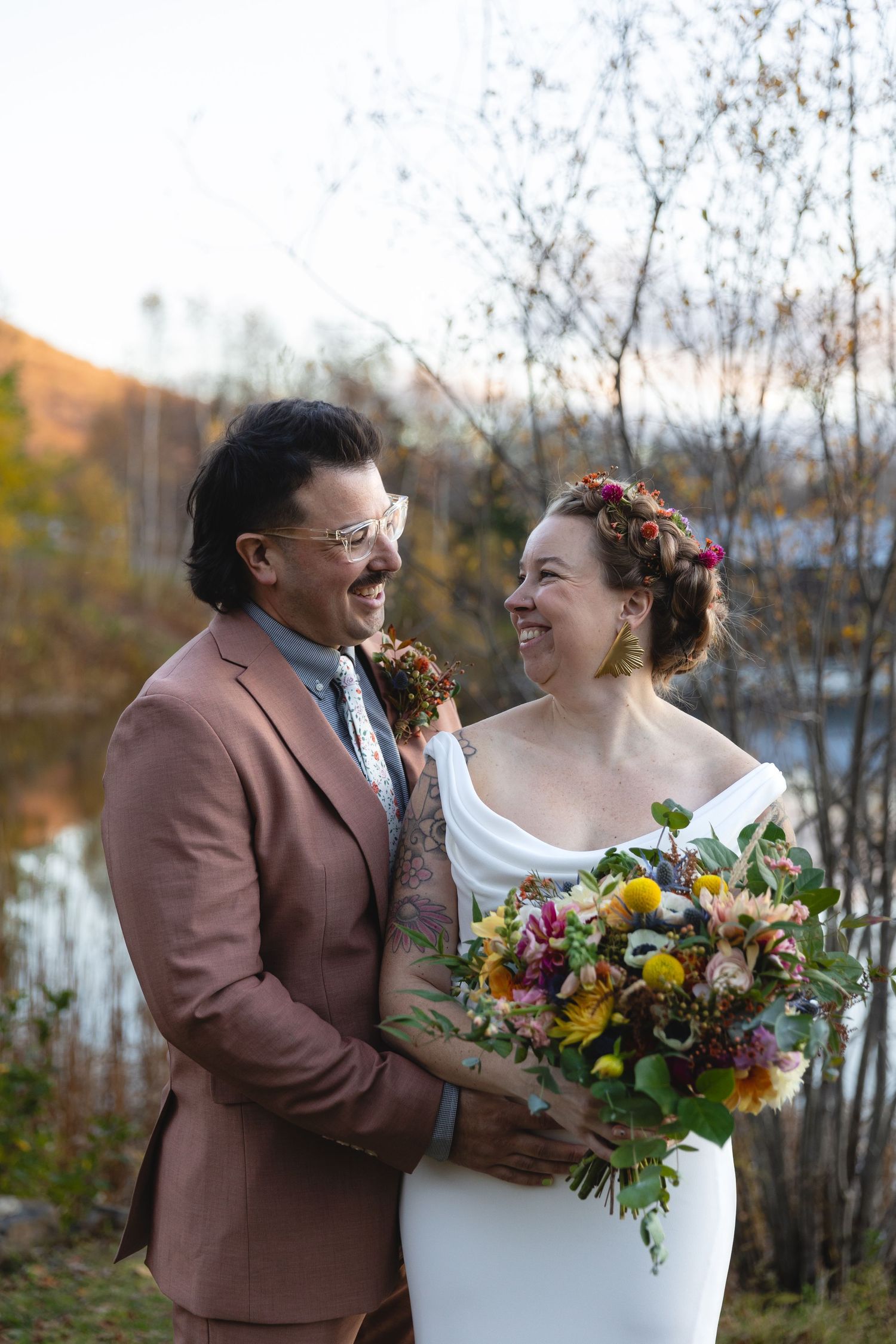 Couple shares intimate moment with colorful fall bouquet by lakeside.