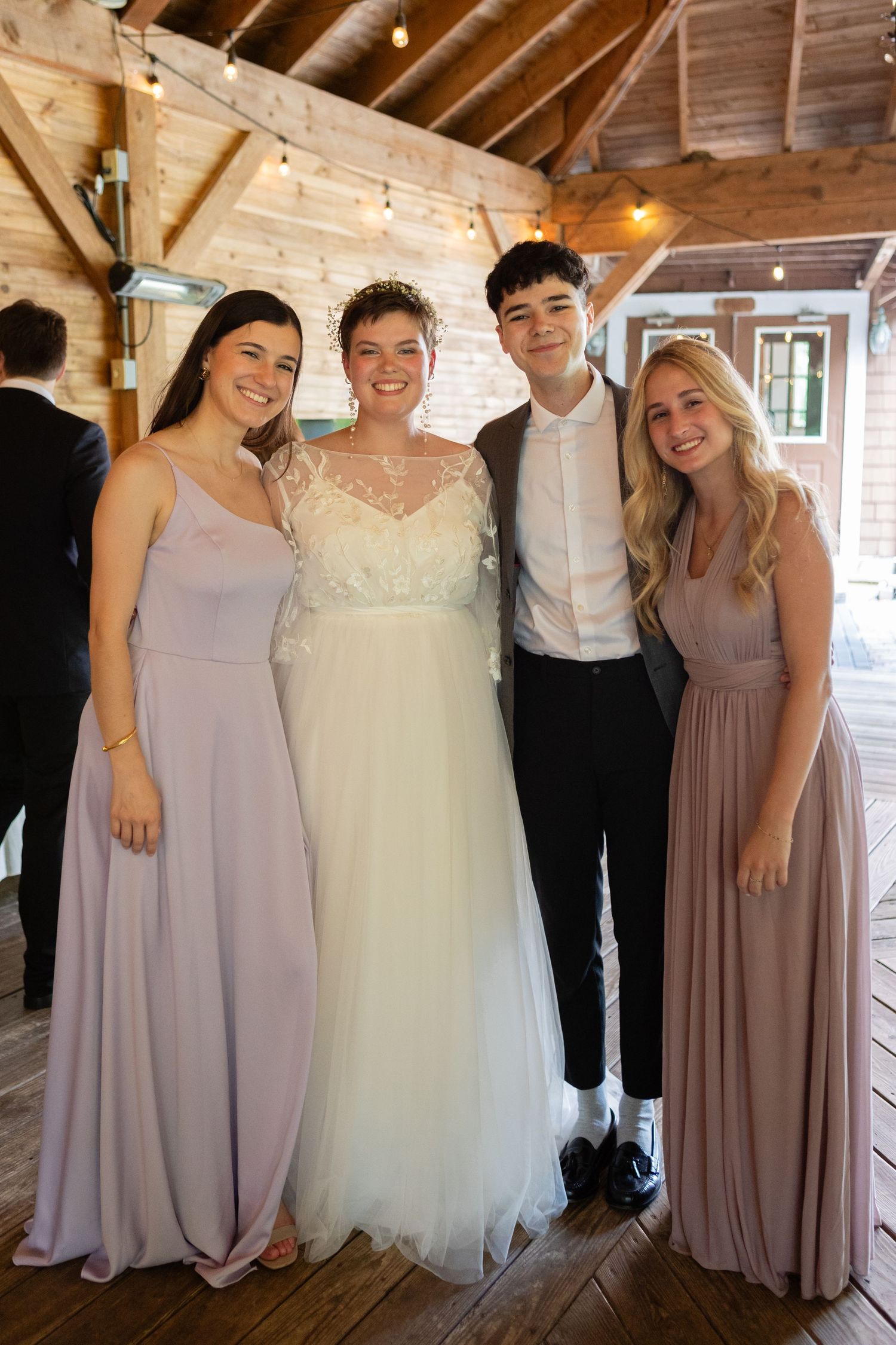 Wedding party members pose together in formal attire inside a rustic wooden venue.