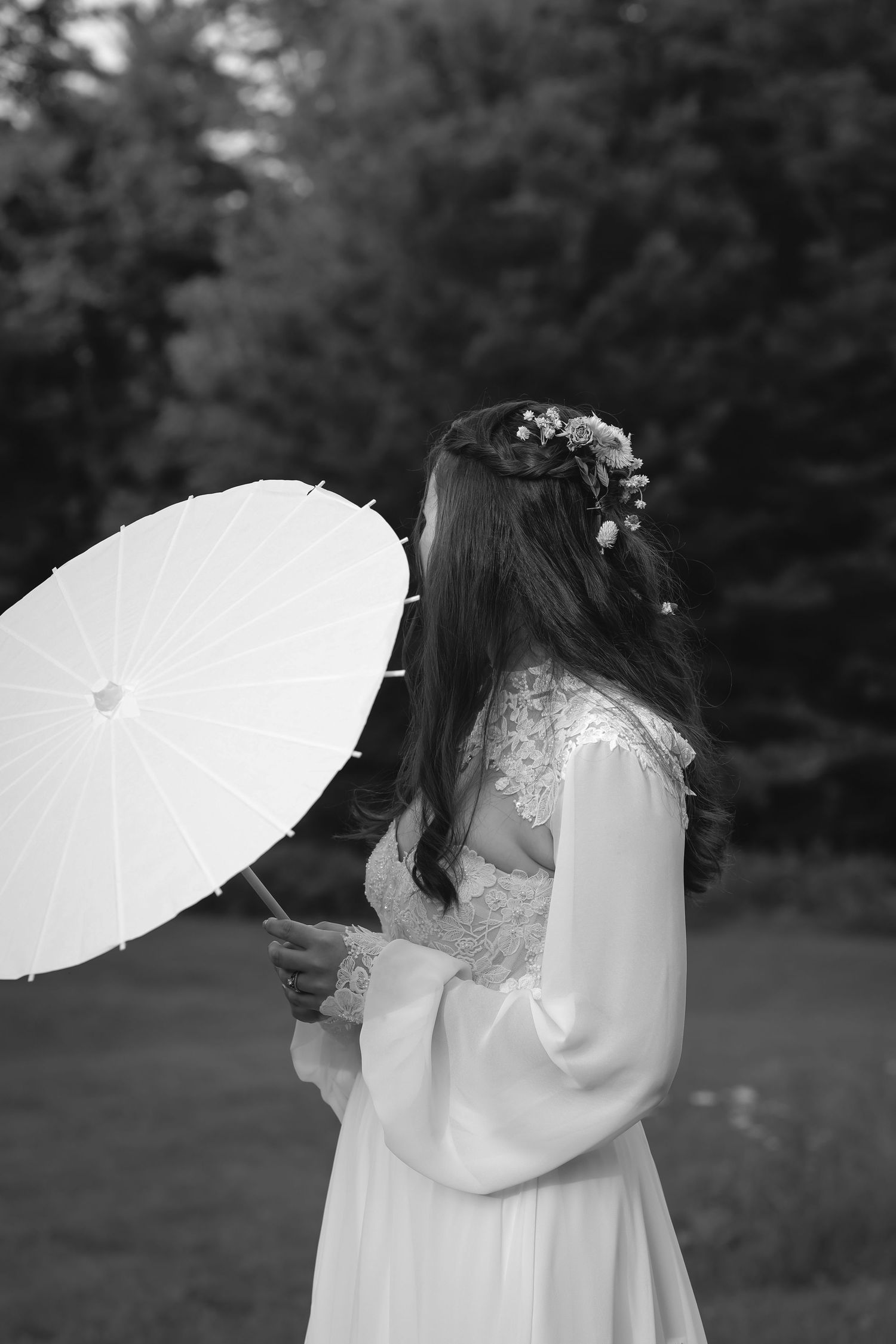 Black and white portrait of bride in lace gown holding white parasol with floral hair crown.