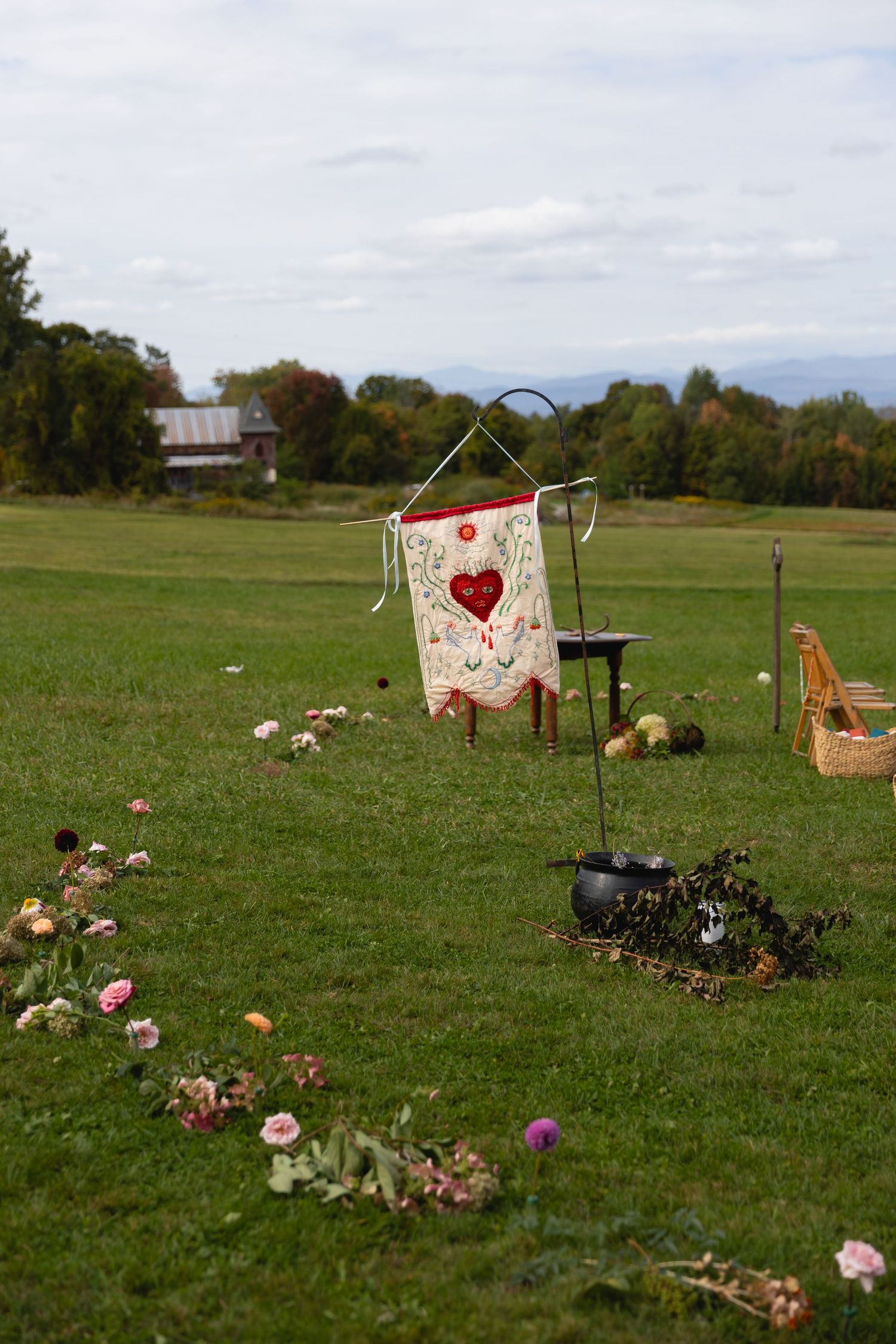 Rustic outdoor wedding ceremony setup with floral aisle, banner, and scenic Vermont countryside backdrop.