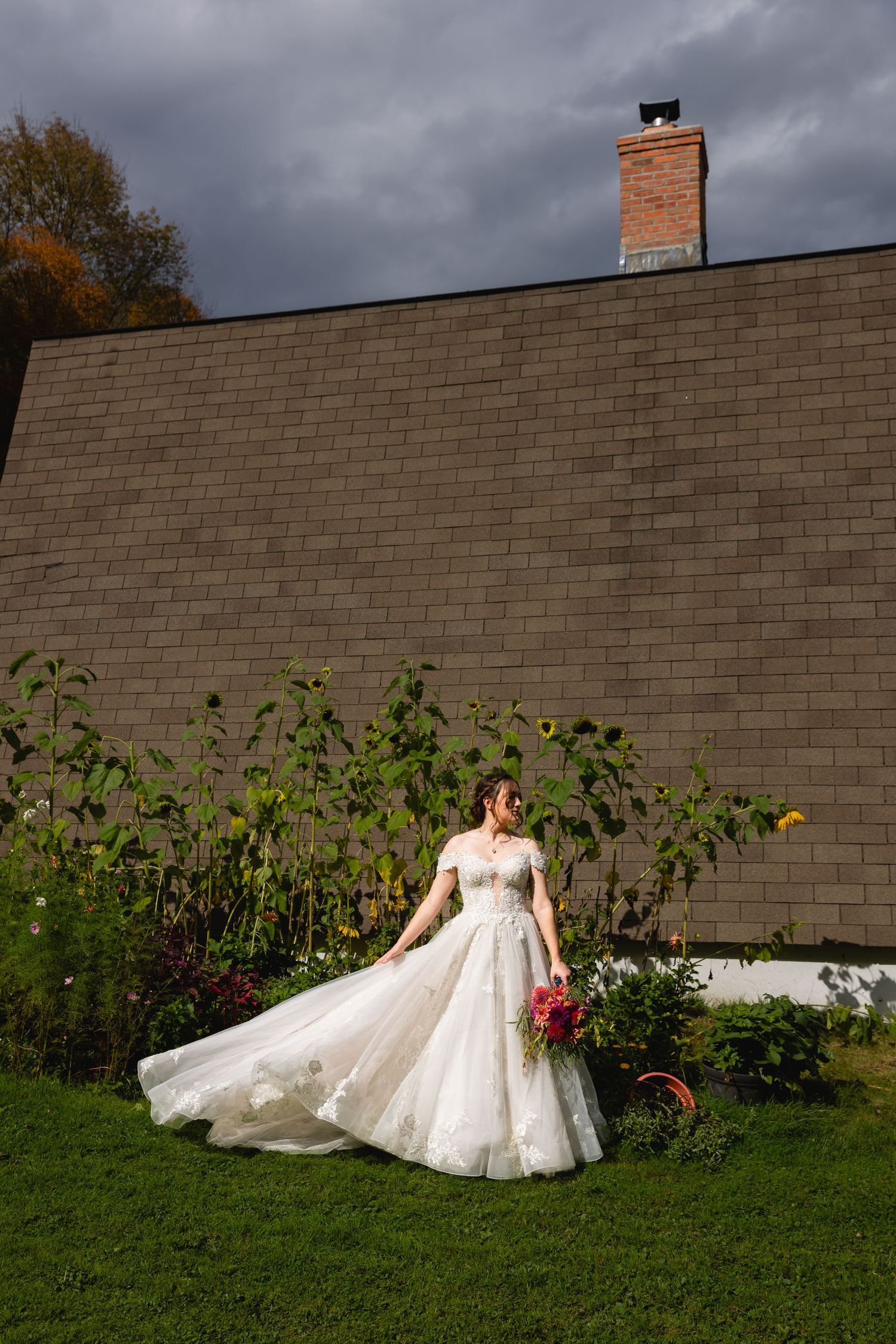 Bride in a white ball gown holding a bouquet poses in front of a brick wall with sunflowers.