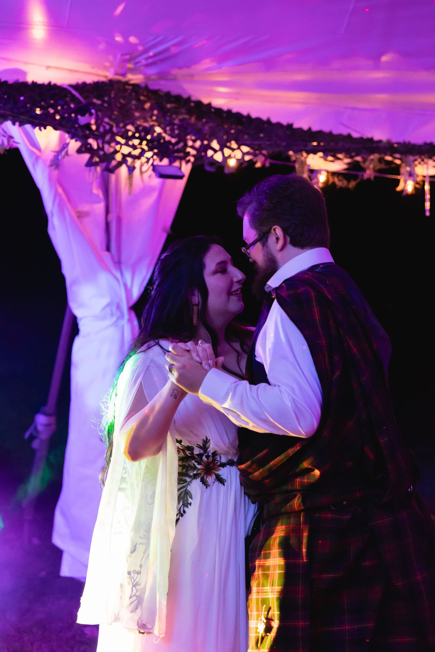 Bride and groom sharing their first dance under purple lights at an outdoor wedding.