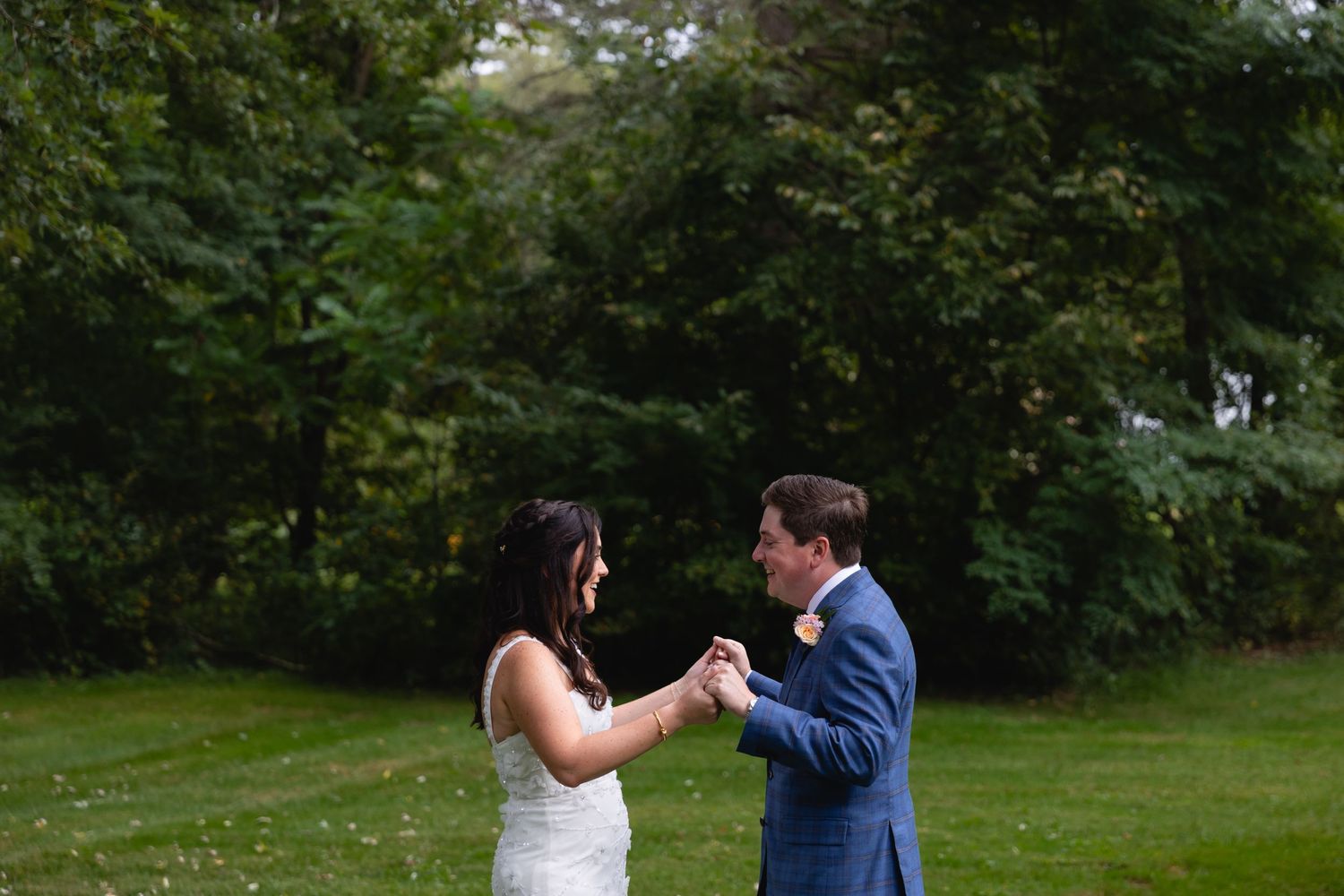A couple dances and smiles together on a lush green lawn with trees in the background.