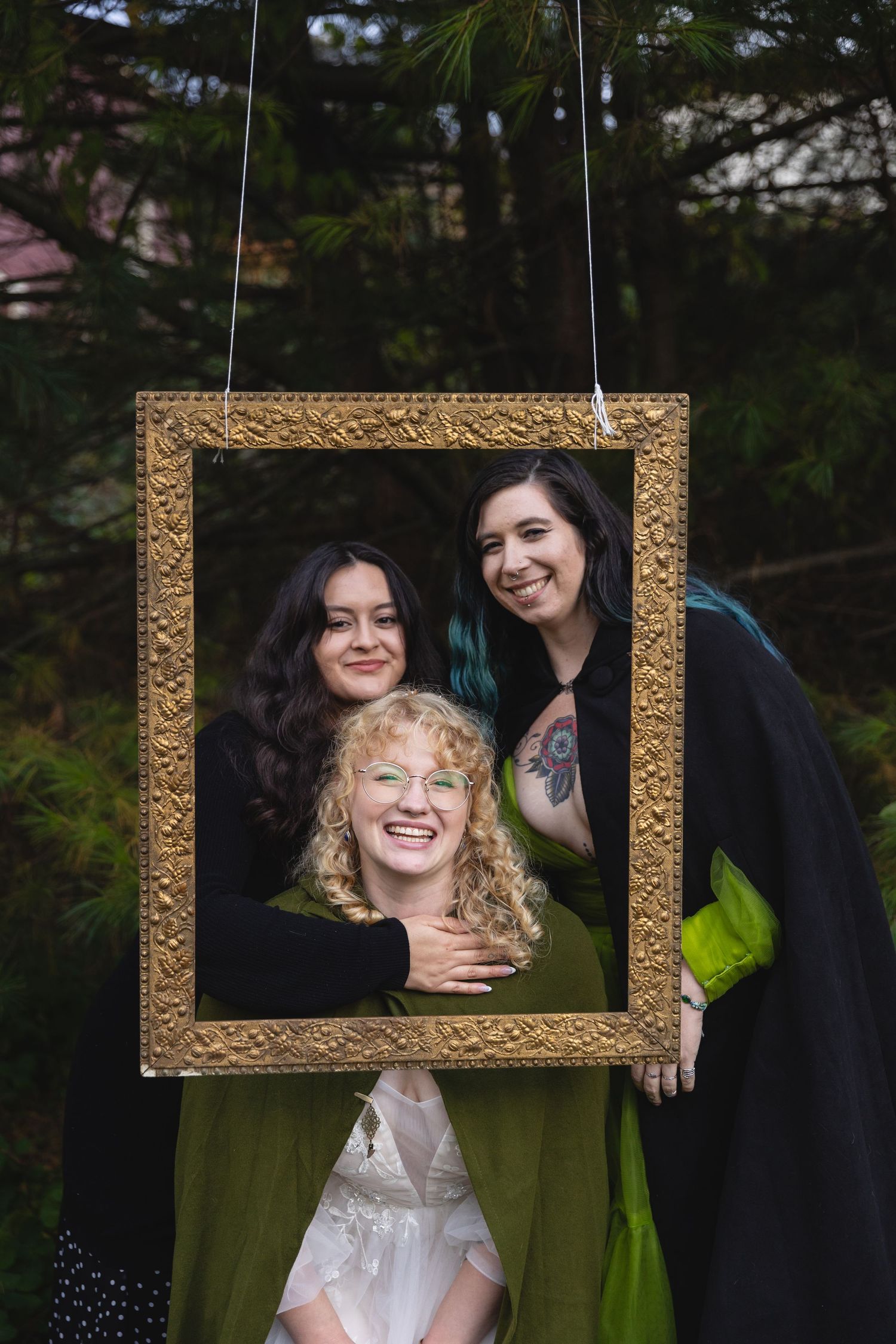 Three friends posing playfully through hanging golden picture frame outdoors.