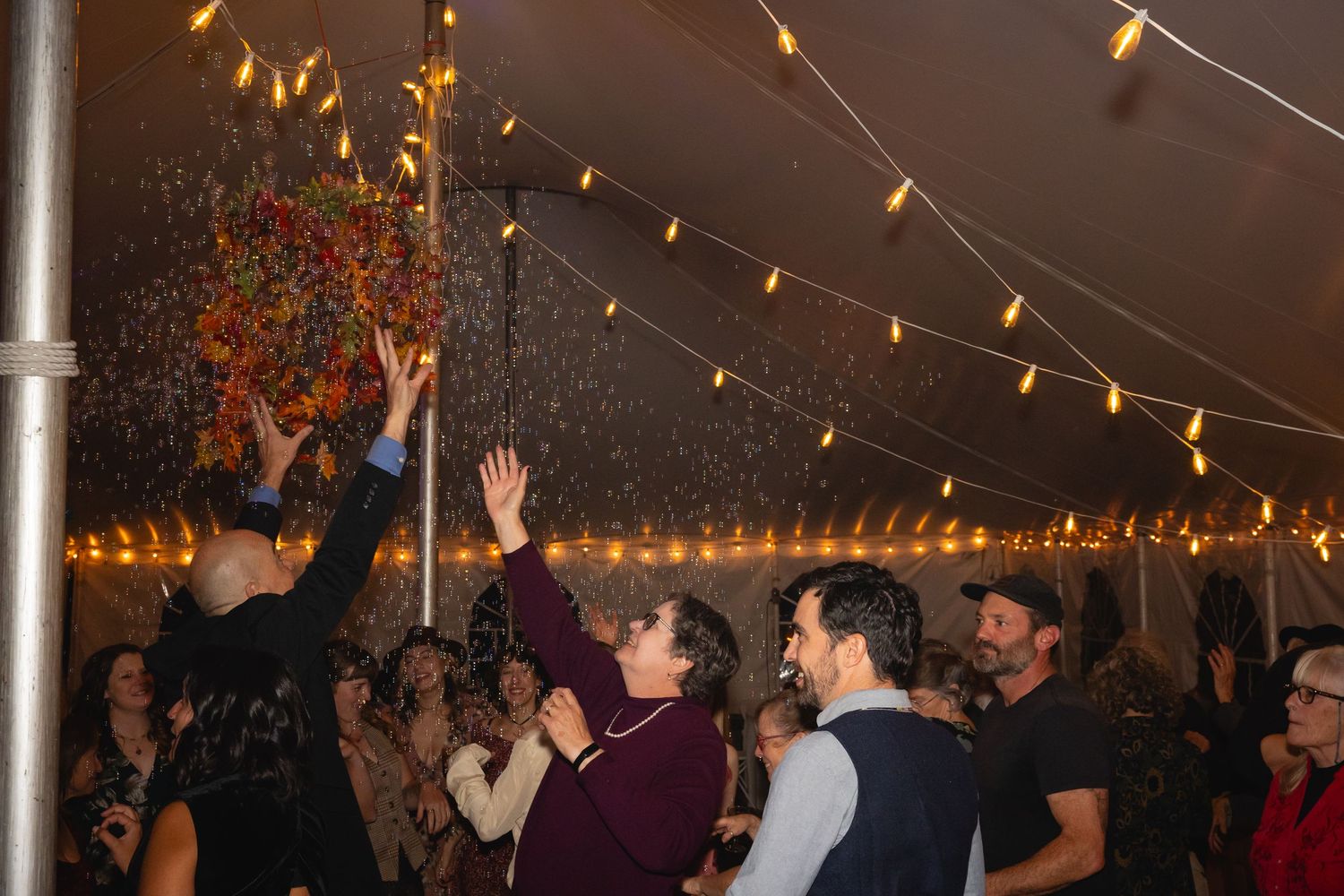 People dancing and celebrating under string lights at an indoor event venue with a festive atmosphere.