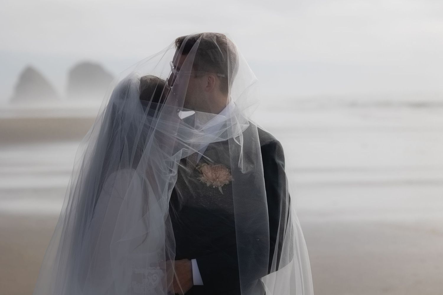A couple embraces and kisses in a romantic moment on a misty beach during golden hour.