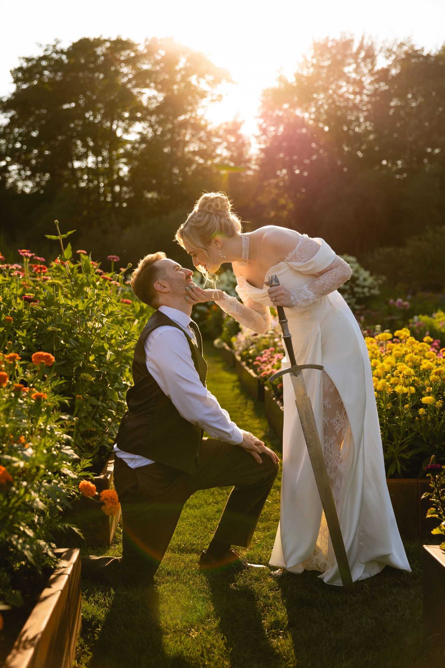 An outdoor wedding ceremony takes place under a wooden gazebo decorated with colorful floral arches and greenery.