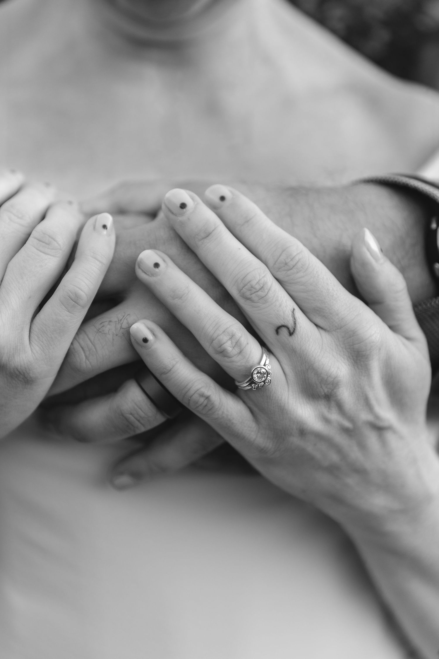 Black and white close-up of hands with small dot nail art and wedding rings.