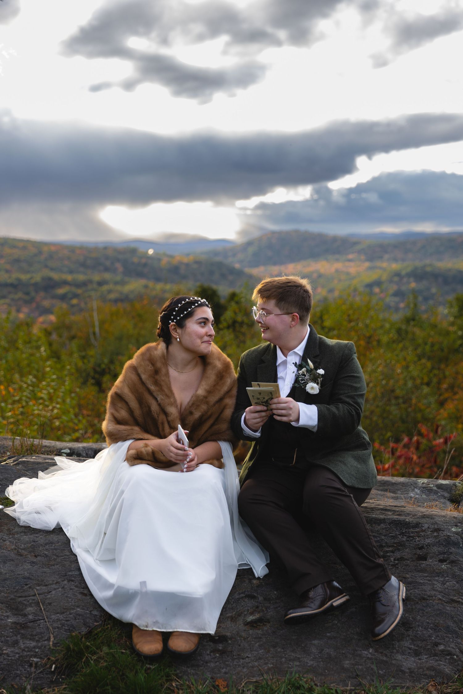 A couple shares an intimate moment while sitting on rocks overlooking a mountain vista.