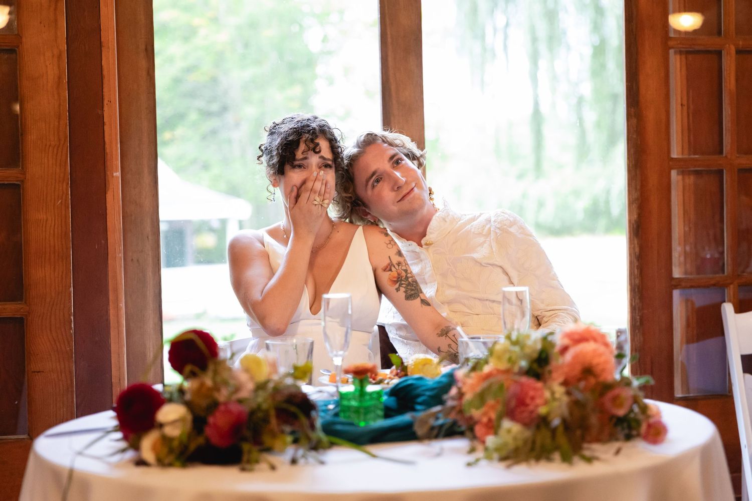 Bride and groom share a joyful moment at their wedding reception table adorned with colorful floral arrangements.