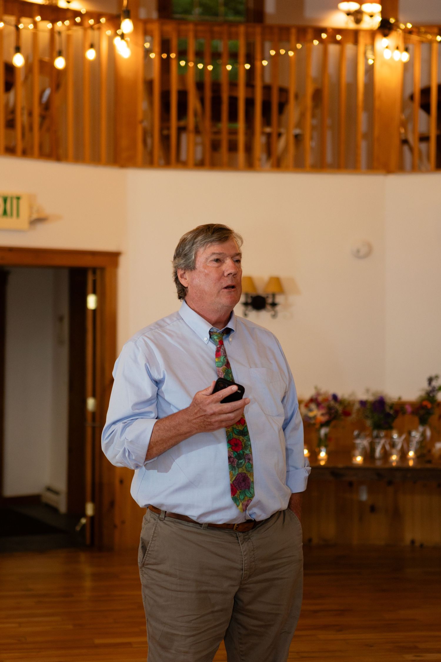 Speaker addressing audience in rustic venue with string lights.