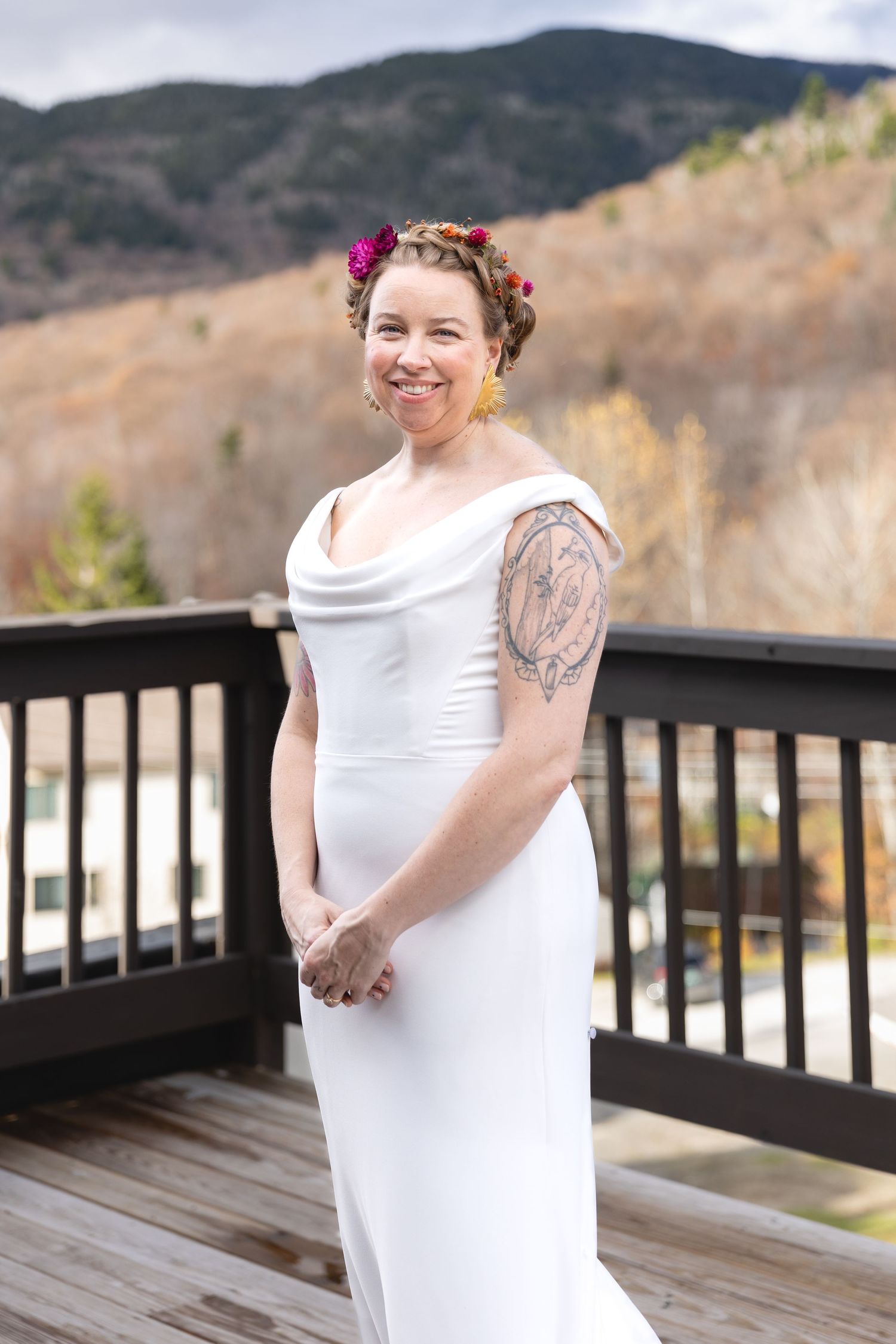 Bride in elegant white dress with floral crown poses on mountain view deck.