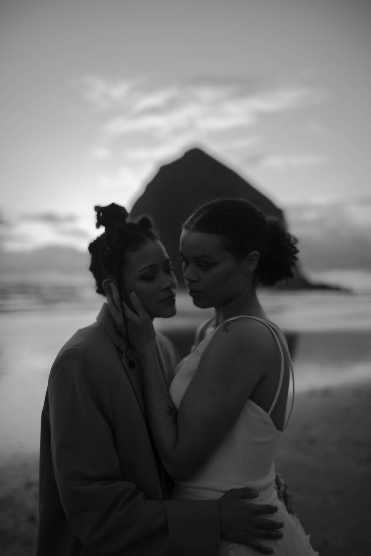 A black and white portrait capturing an intimate moment between newlyweds on the beach.