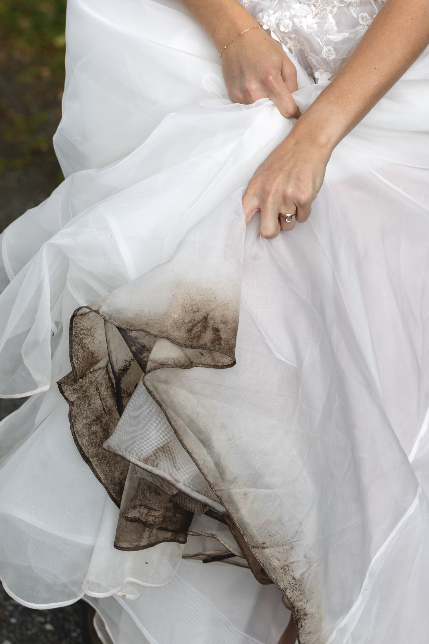 Muddy hem of white wedding dress showing through layers of tulle fabric.