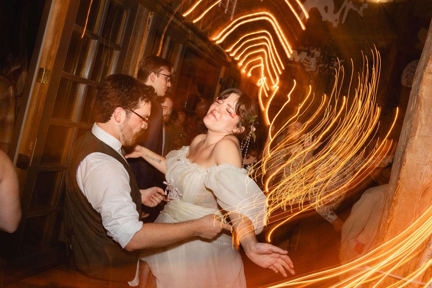 A couple dances together while orange light trails swirl around them creating a magical atmosphere at their wedding reception.