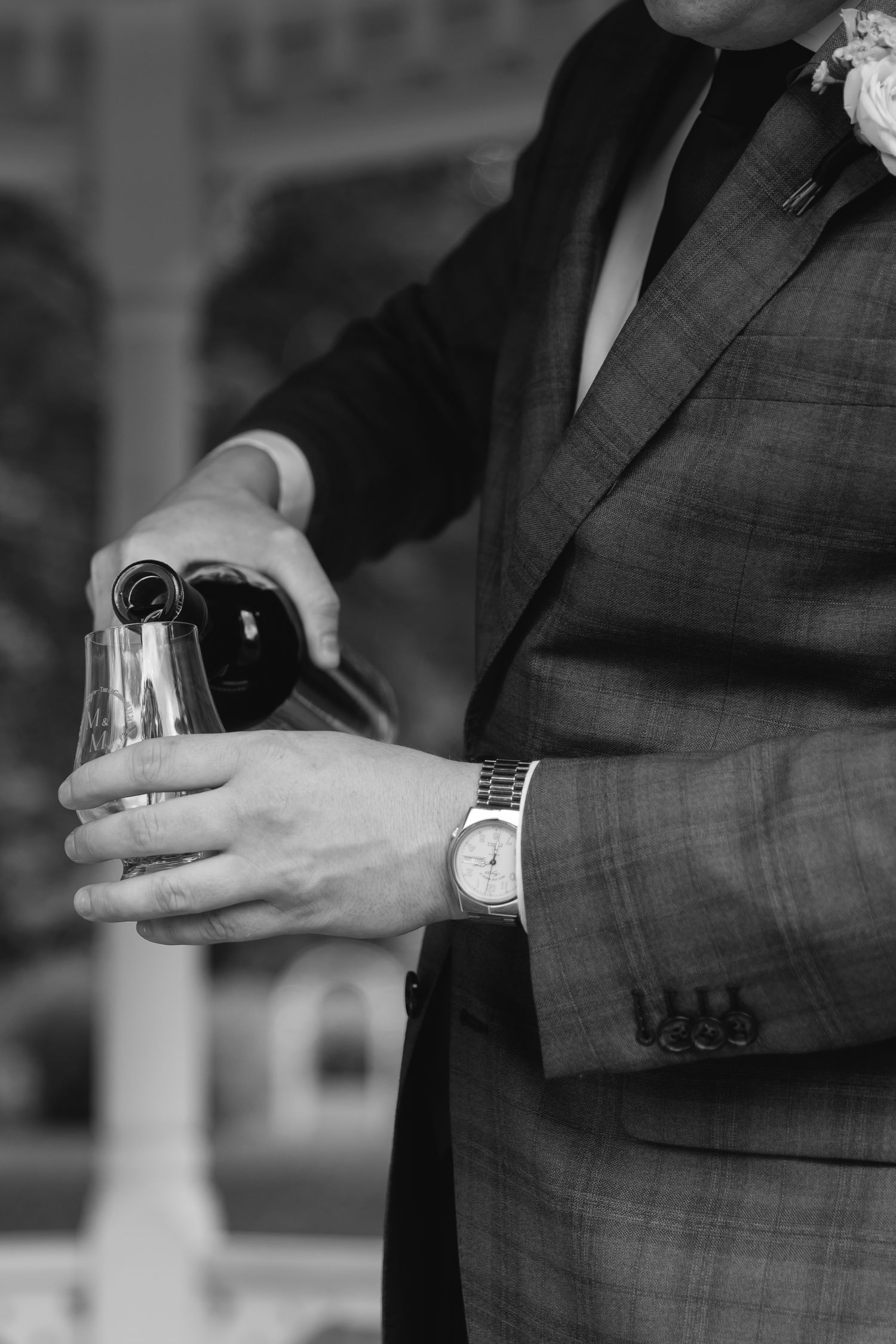 Black and white image of someone in a suit pouring wine into a glass while wearing a wristwatch.
