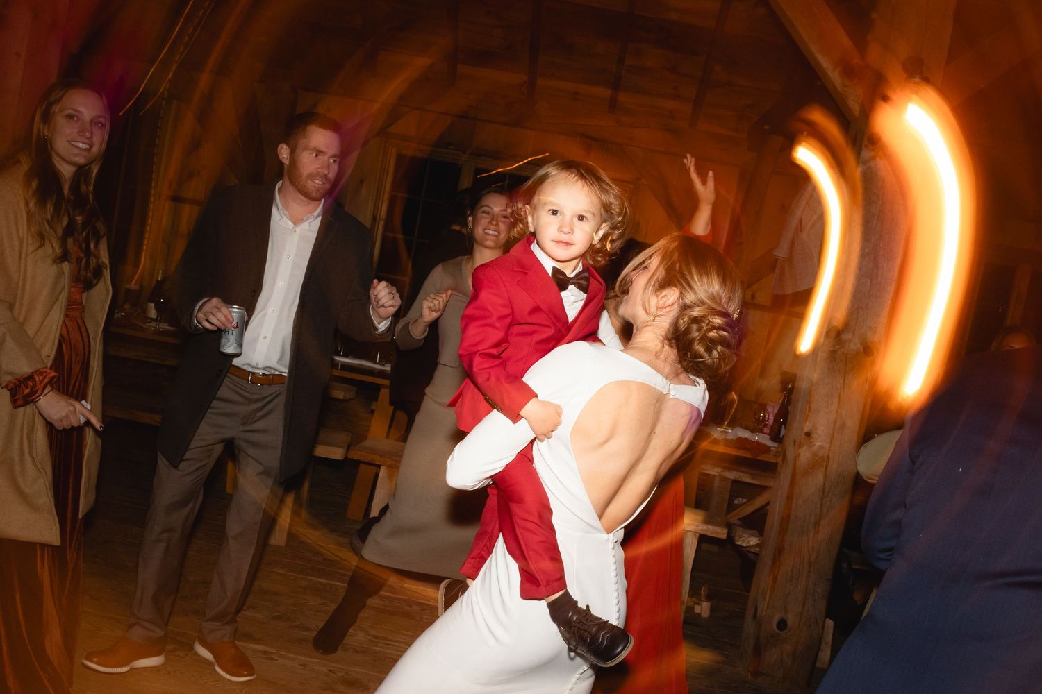 Dance party at a wedding reception with people dancing and laughing in a warmly lit indoor venue.