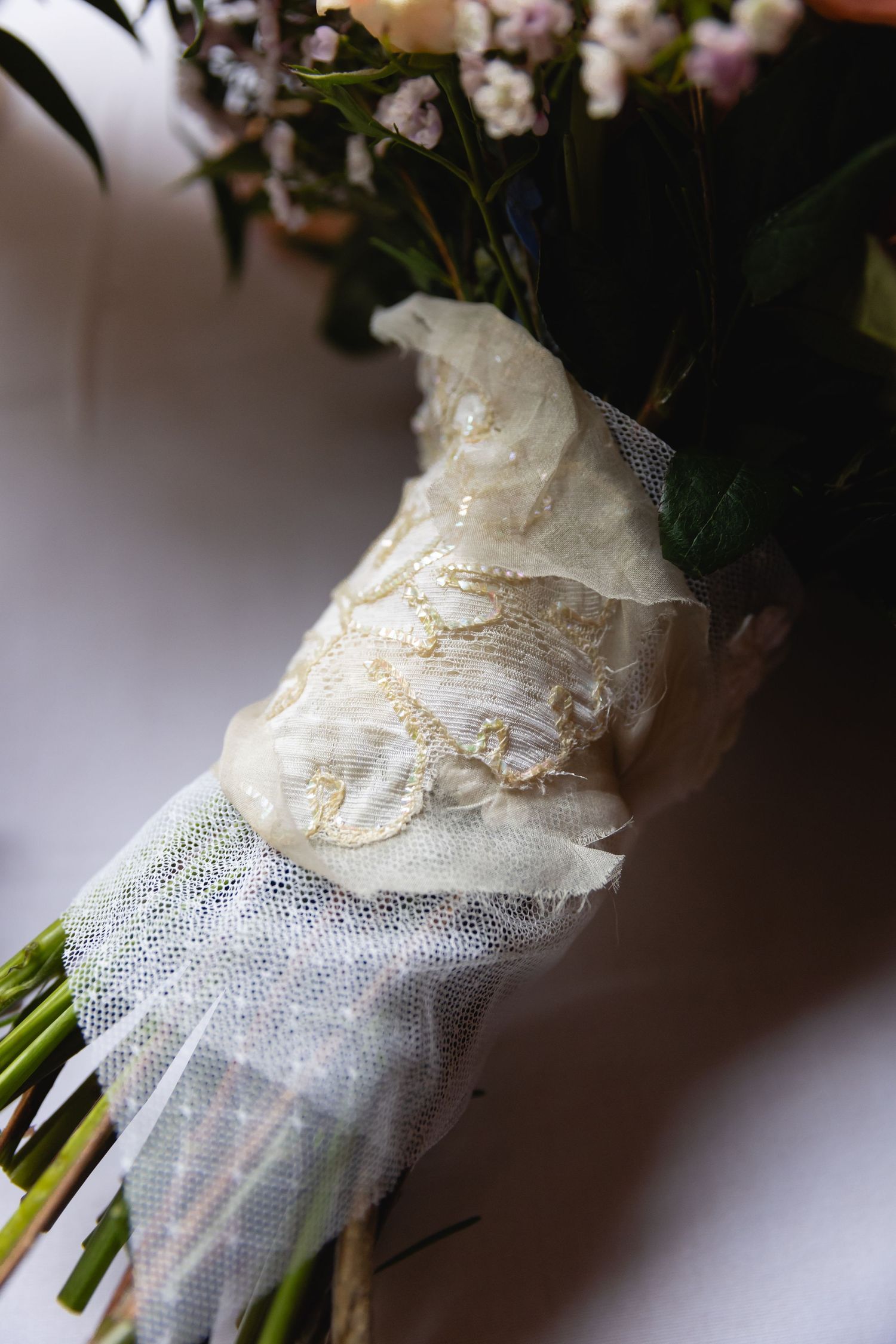 A bridal bouquet wrapped in delicate white lace and tulle fabric showing intricate vintage-style details.