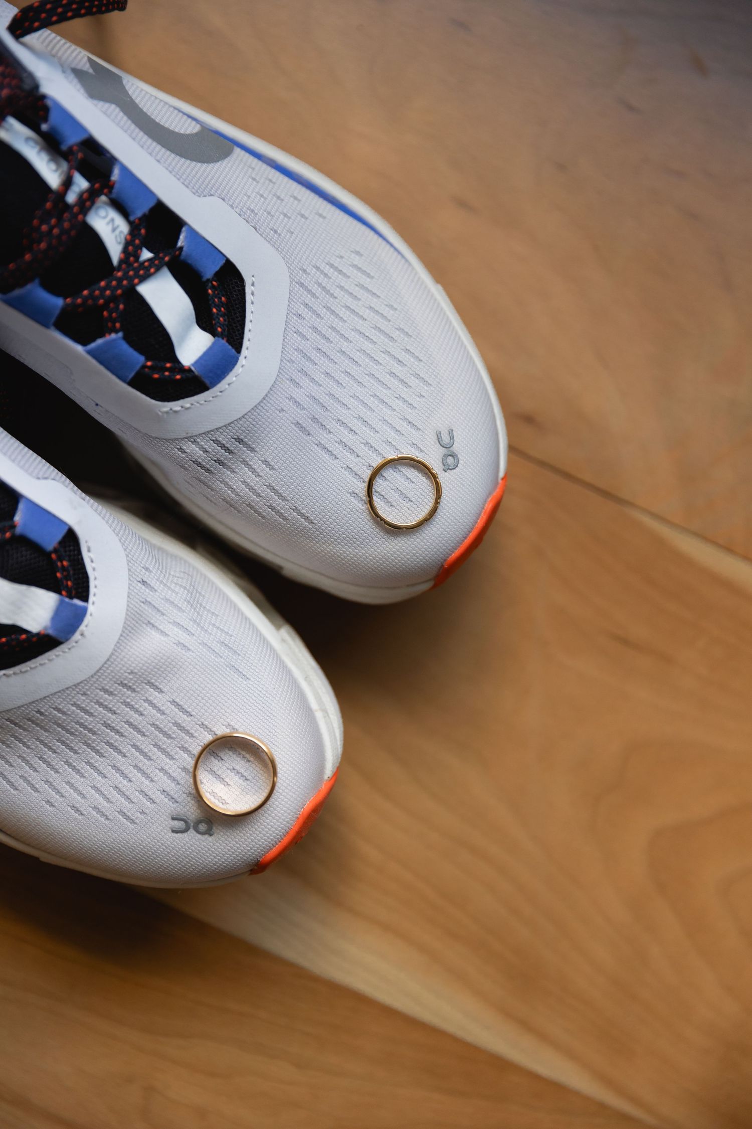 White athletic running shoes with orange accents and black laces displayed on wooden floor surface.