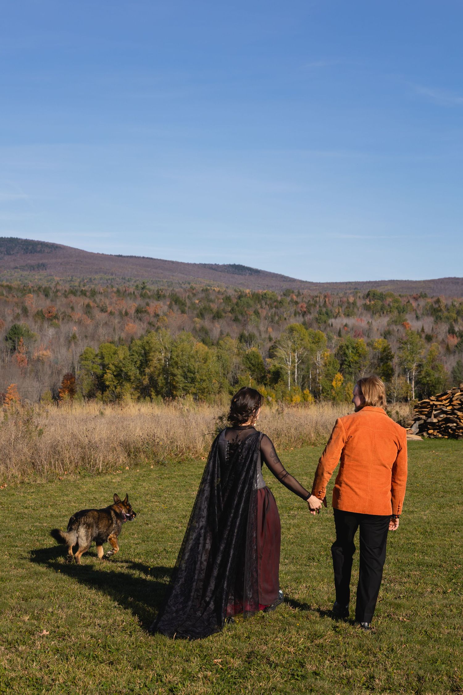People walk together through an autumn field with mountains and colorful fall foliage in the background.