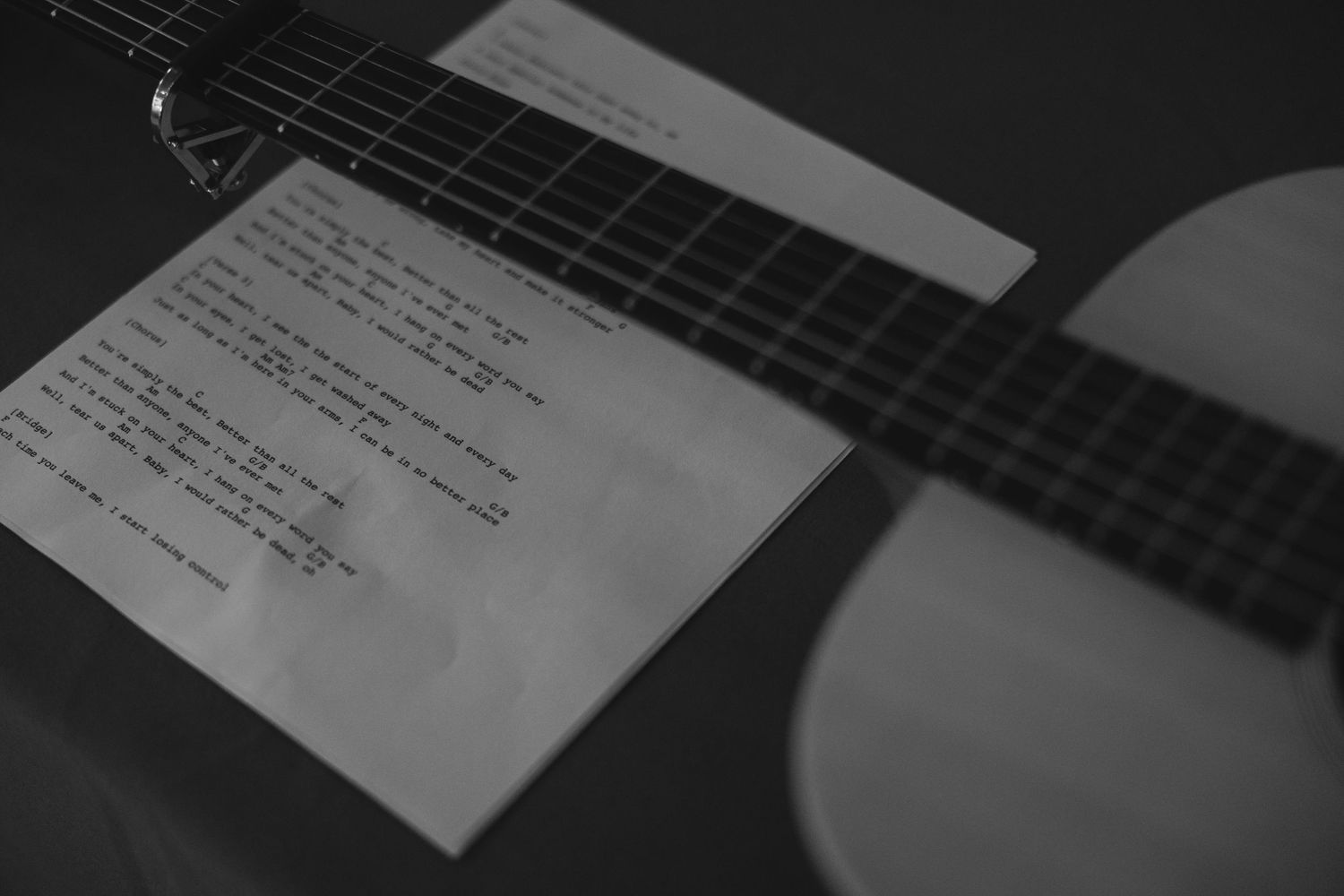 Sheet music resting on the neck of a black acoustic guitar in dim lighting.