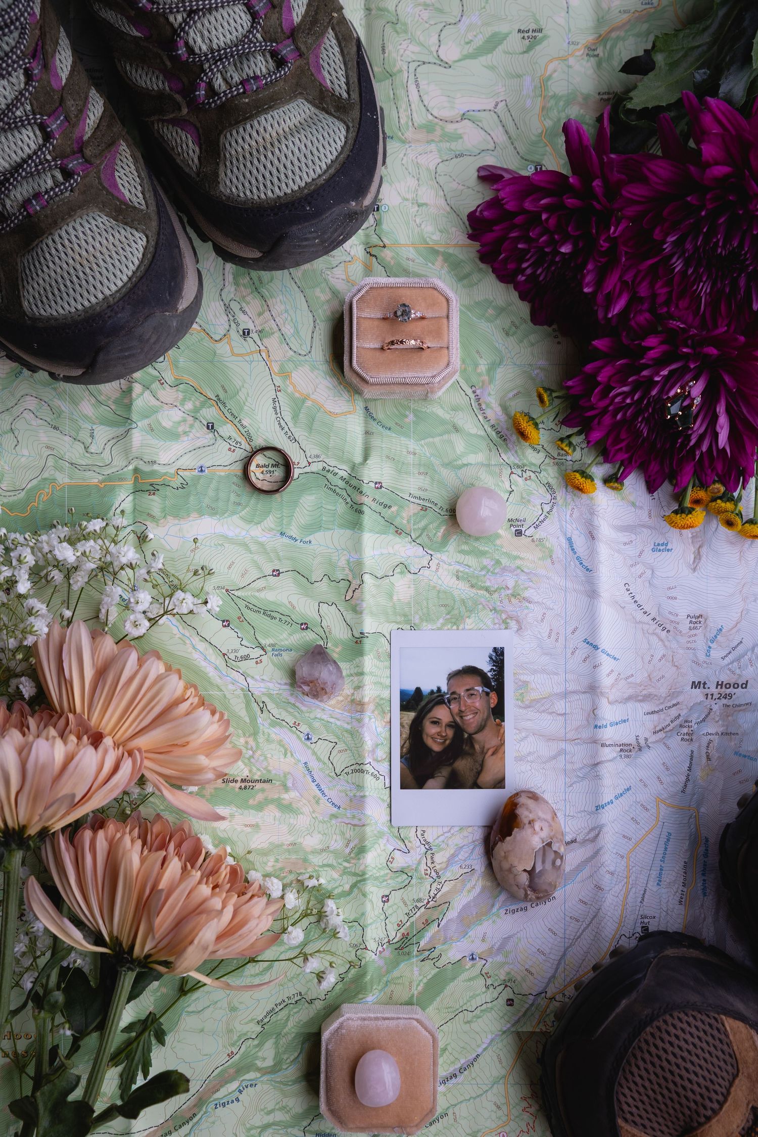 Flatlay arrangement of shoes, flowers, photos and personal items on a map background with pink and purple accents.