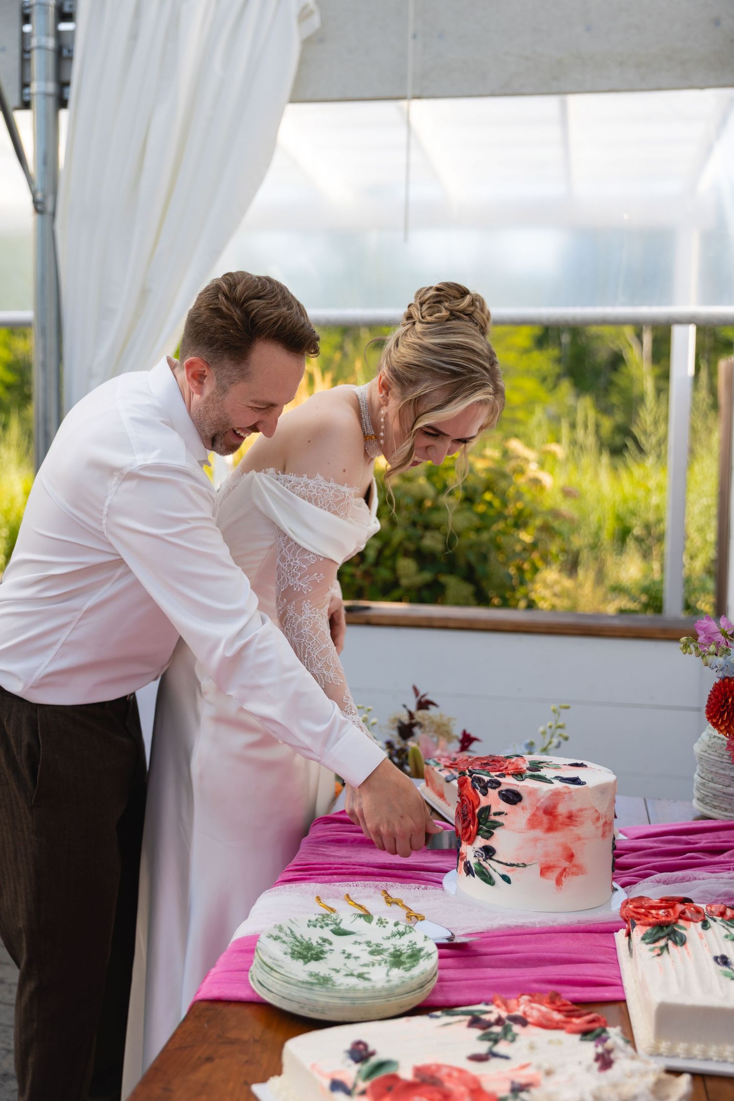 Wedding cake cutting ceremony with a white-dressed couple at an outdoor reception under a white tent.