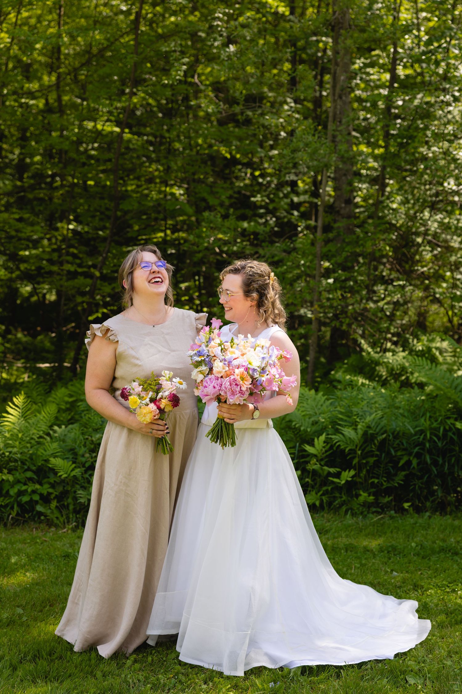 Two people in wedding attire share a joyful moment together while holding colorful floral bouquets in a lush garden setting.