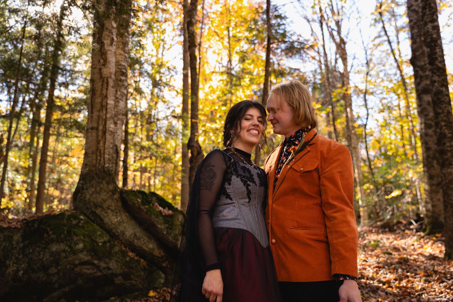Couple walking together through autumn forest with golden sunlight filtering through trees during fall photoshoot.