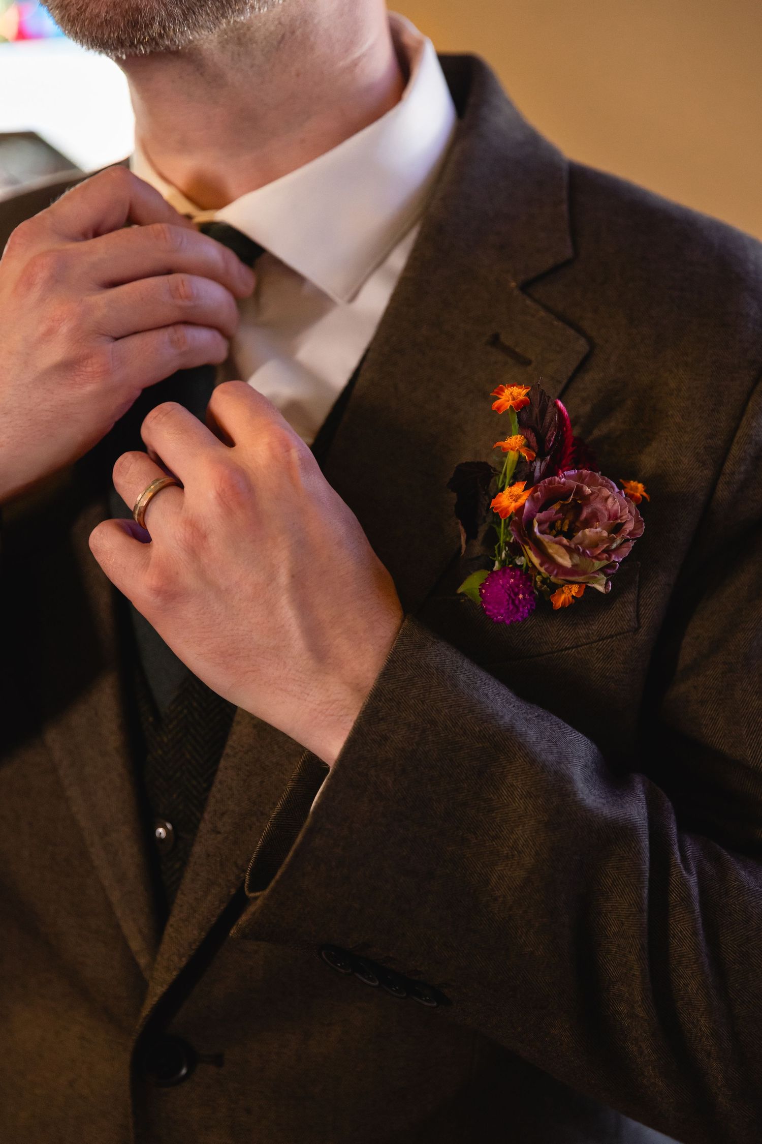 Close-up shots of a dark suit lapel with vibrant orange and purple floral boutonniere being adjusted.