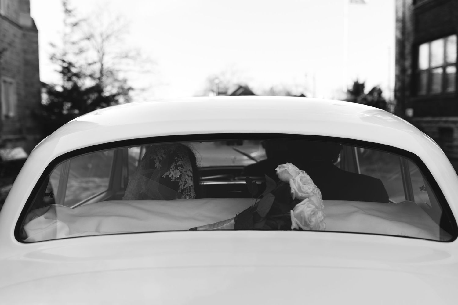 A black and white photo showing the rear window of a vintage car with people sitting inside.
