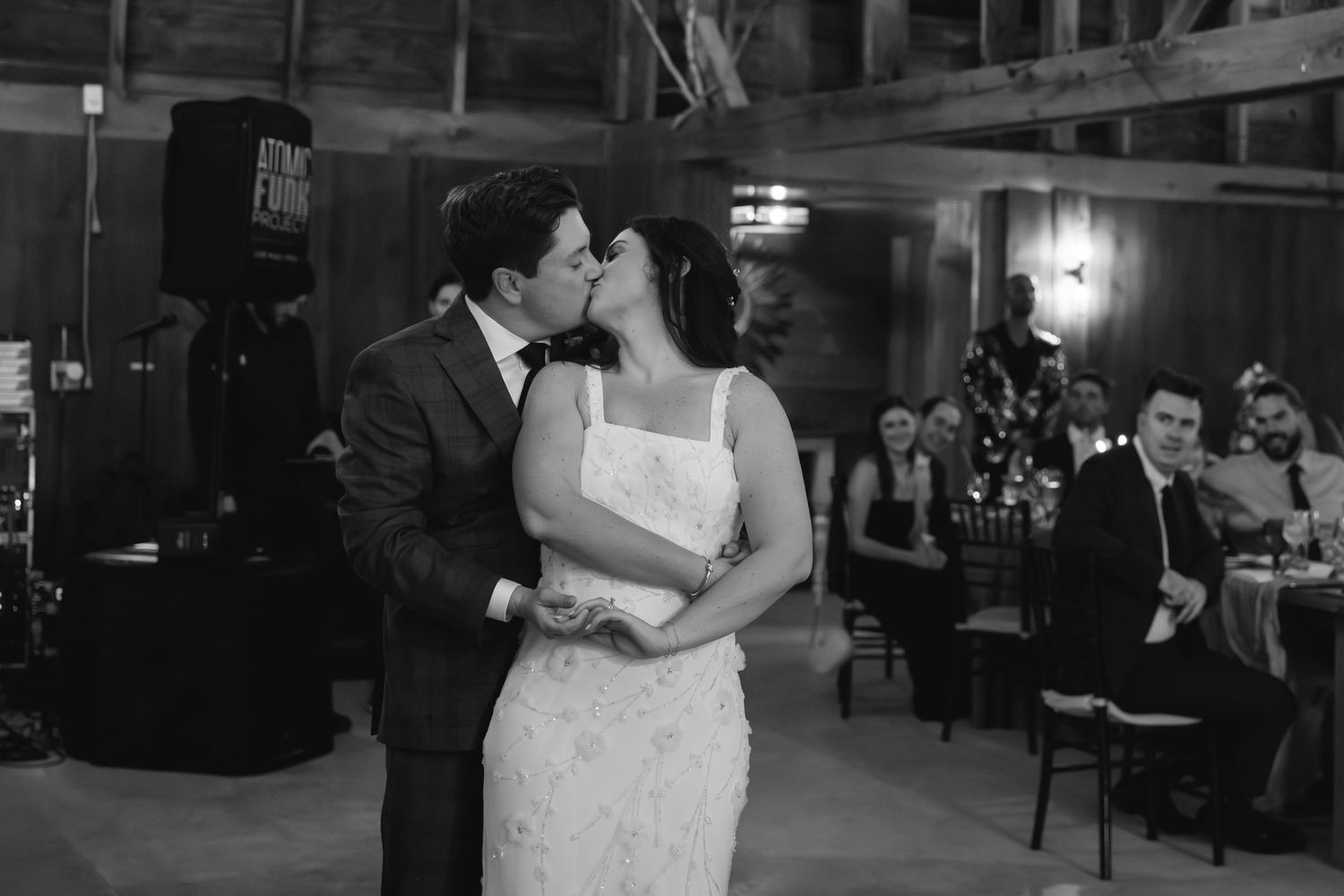 A couple shares their first dance as newlyweds in a romantic black and white moment on a rustic venue dance floor.