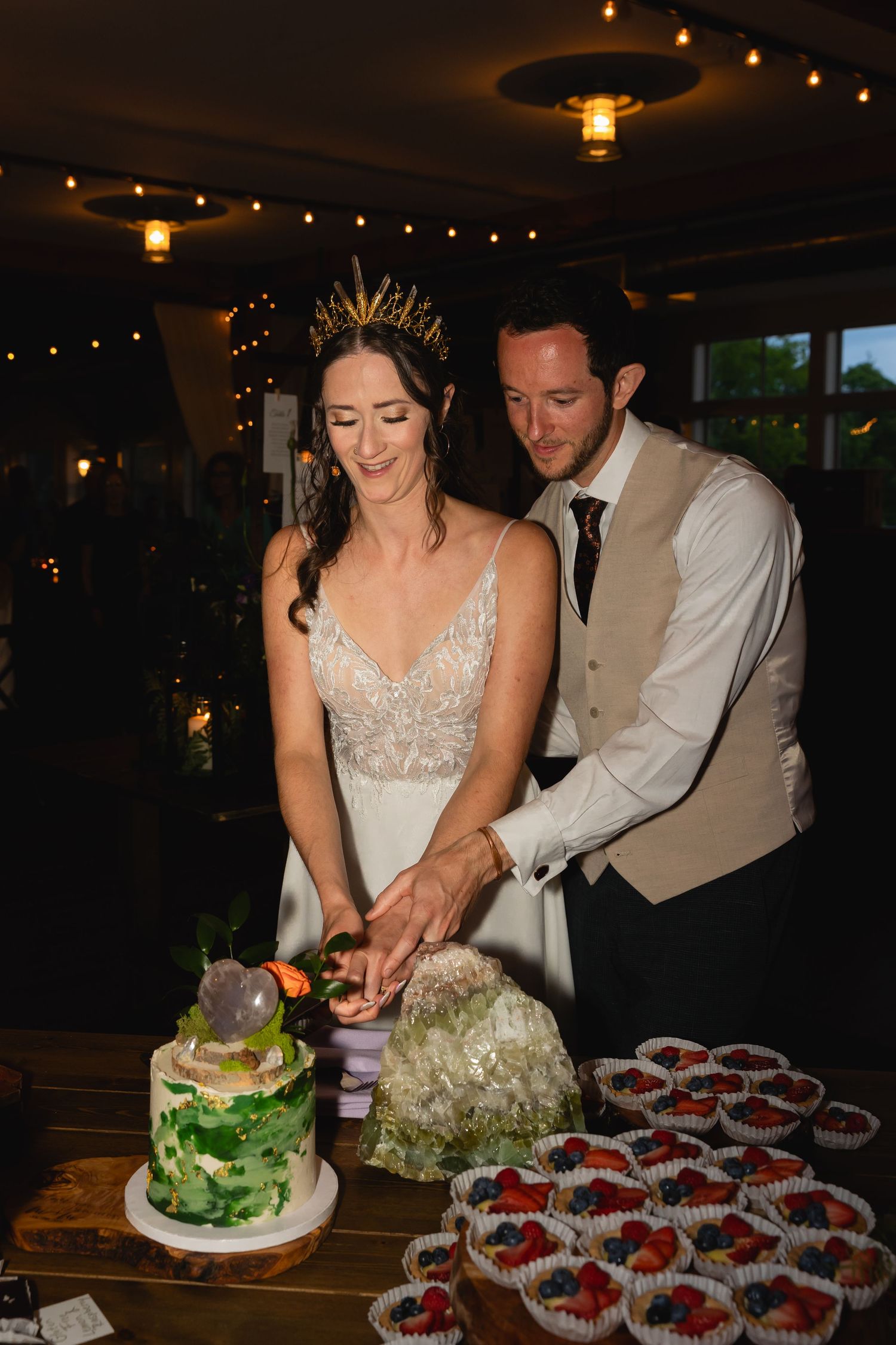 Couple cutting elegant green and white wedding cake at dessert table.