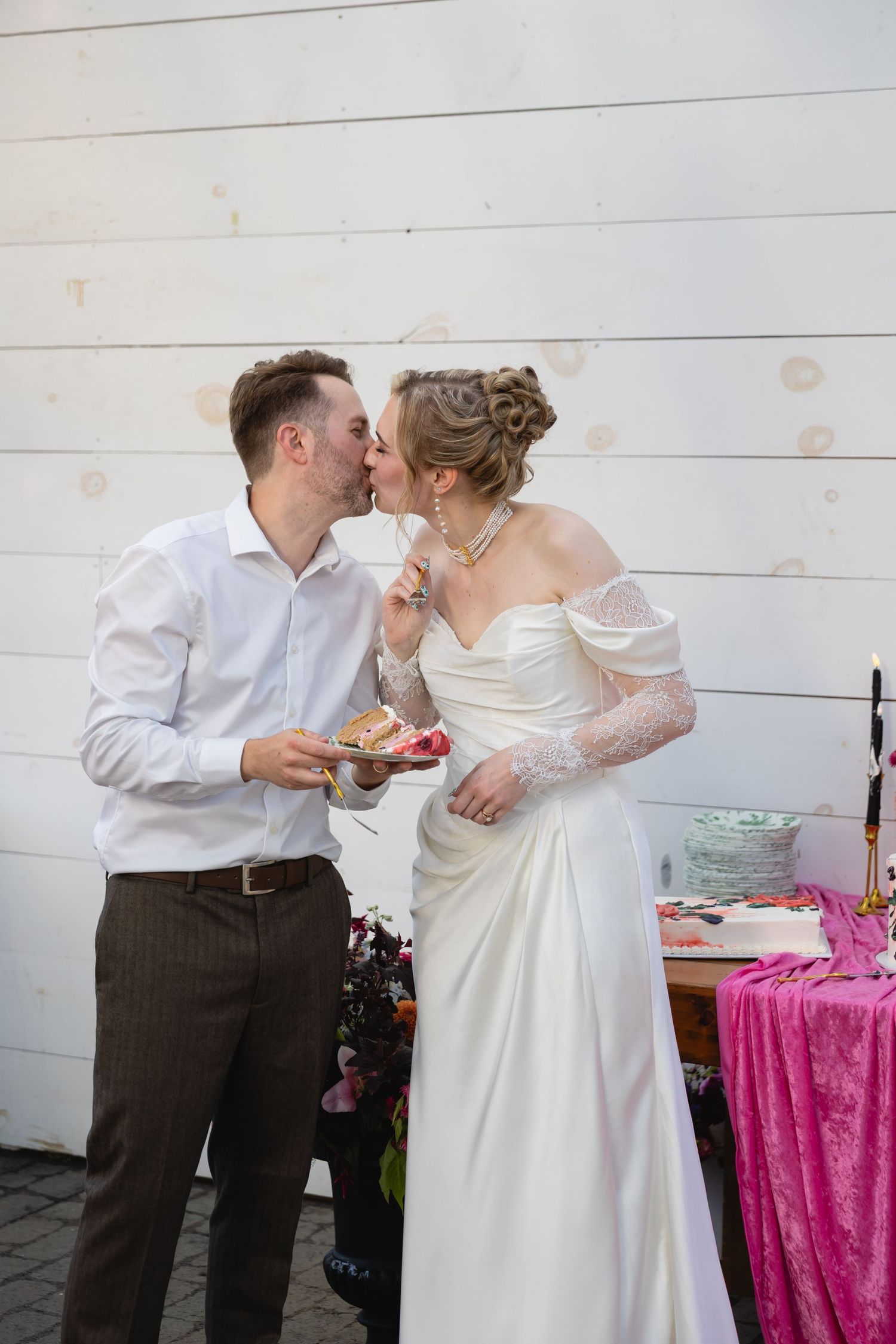 A couple in wedding attire shares a playful moment while eating cake at their reception.