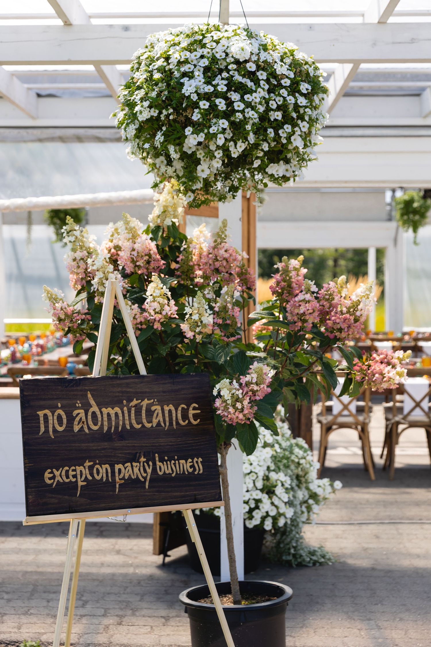 Black chalkboard signs with handwritten text are displayed among potted white and pink floral arrangements in a garden setting.